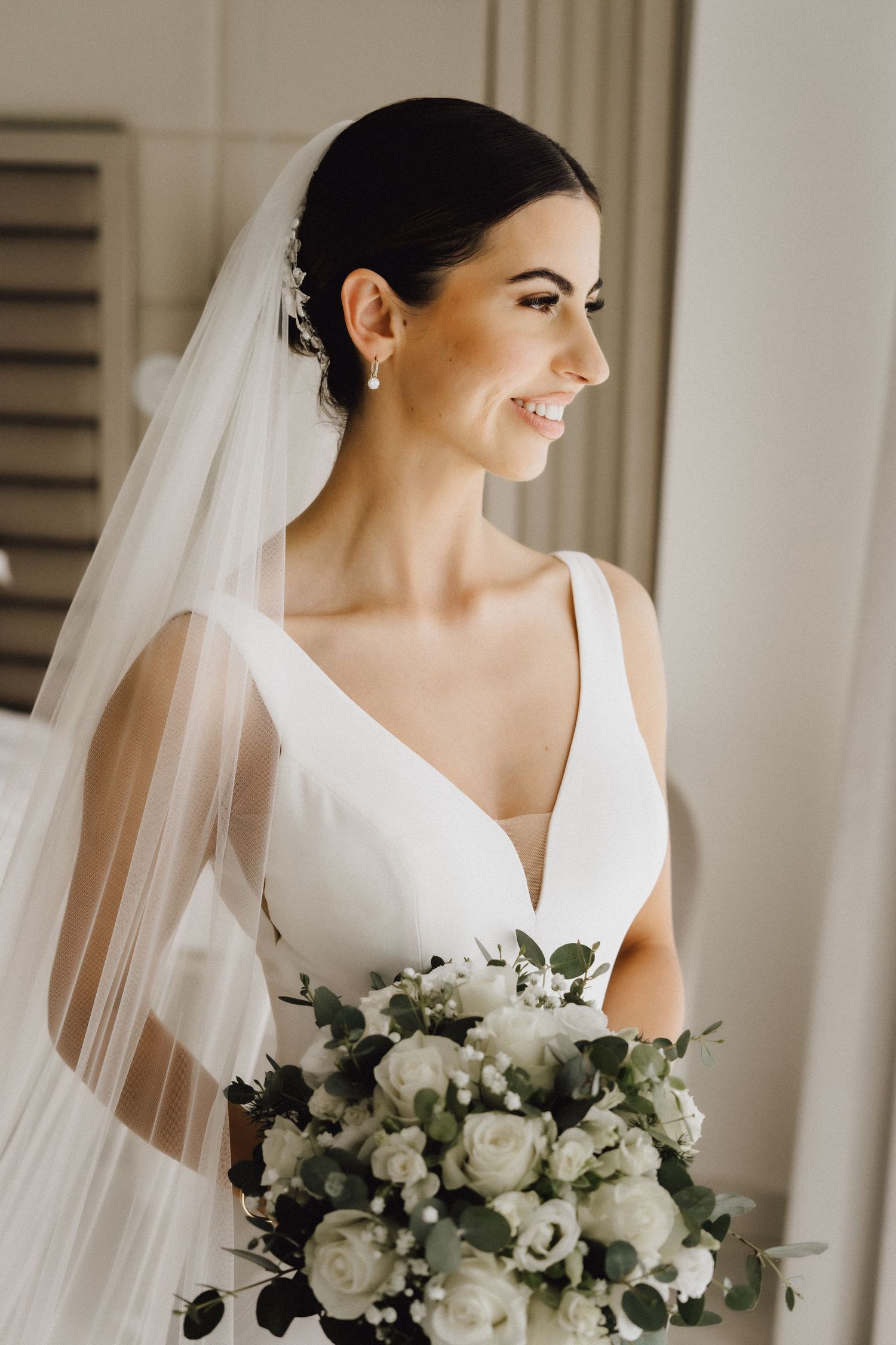 Side view of bride in classic V-neck wedding gown with sheer veil and white floral bouquet.