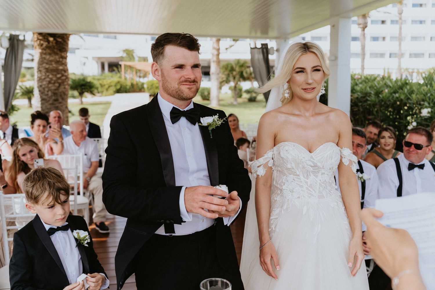 Outdoor wedding ceremony under covered patio with ring bearer standing nearby.