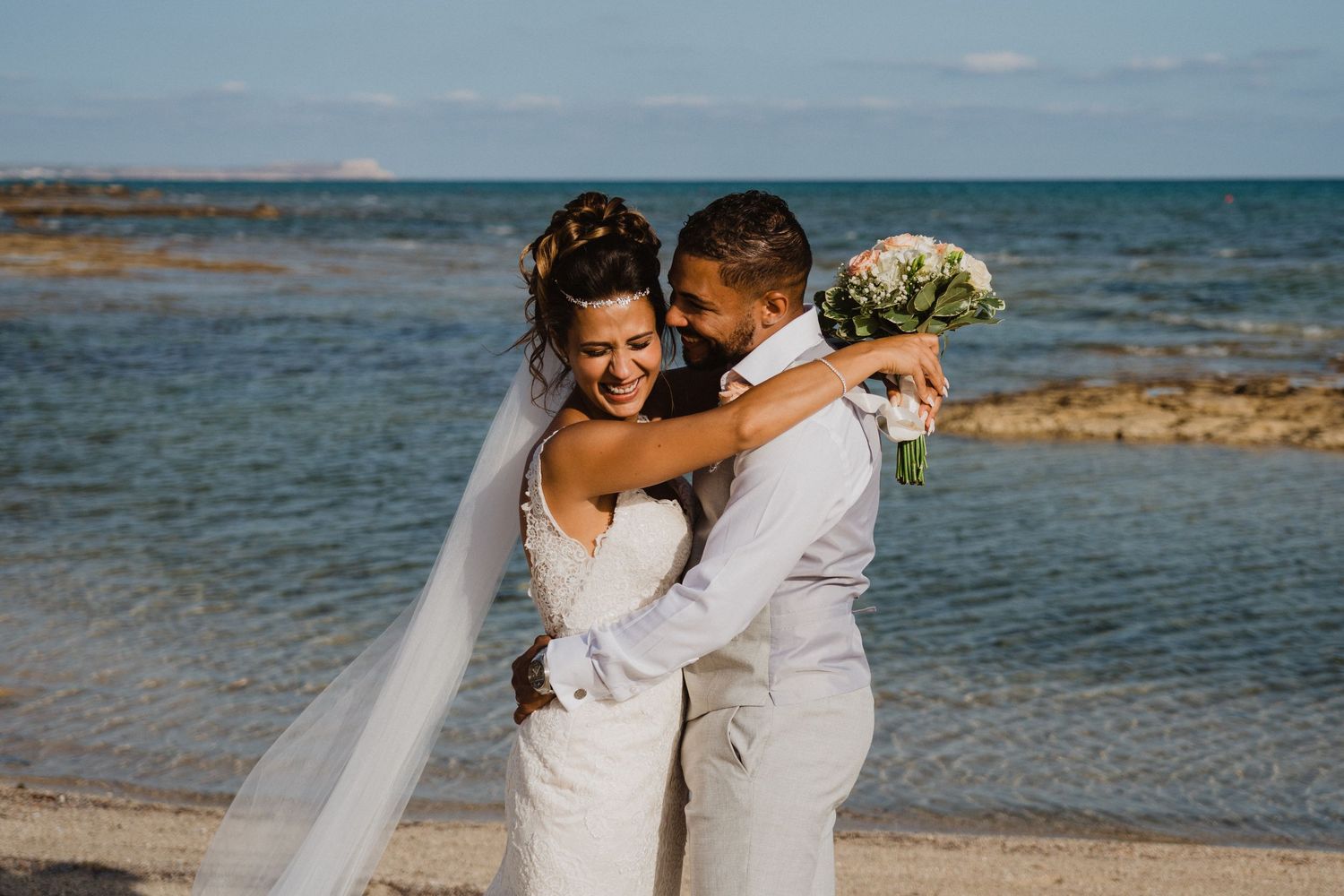 Joyful beach wedding celebration with couple embracing by turquoise ocean waters.