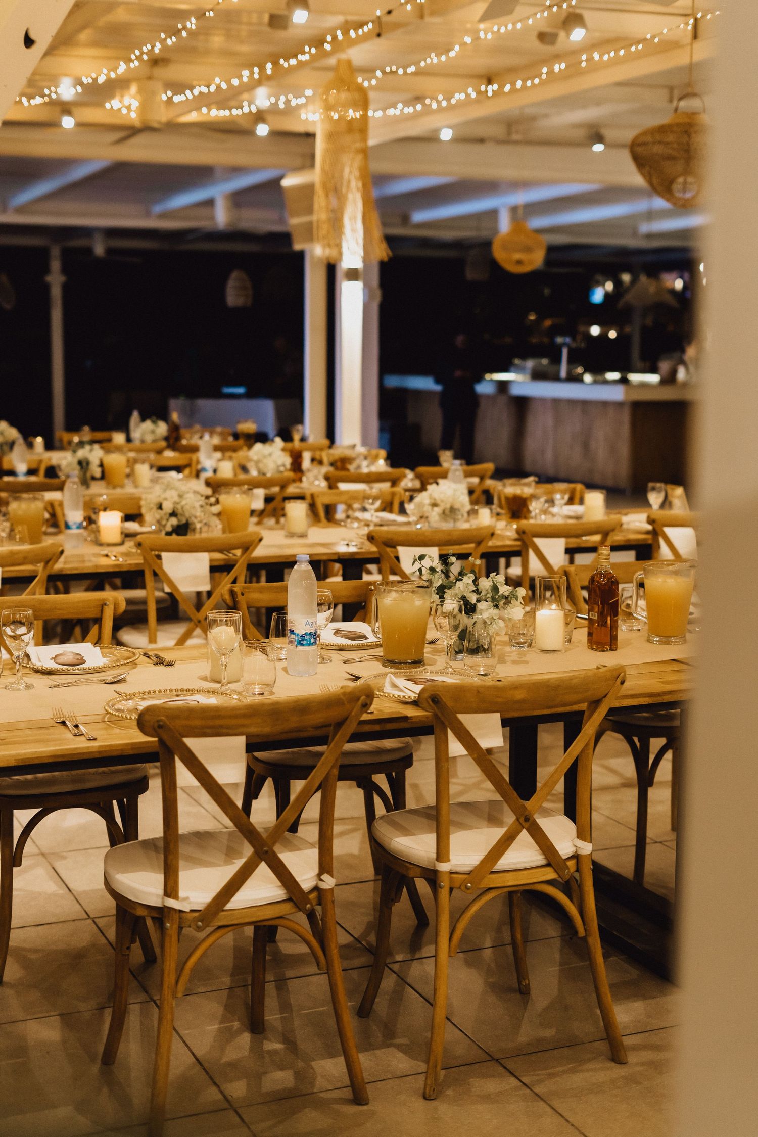 Rustic wedding reception tables with cross-back chairs and warm ambient lighting.