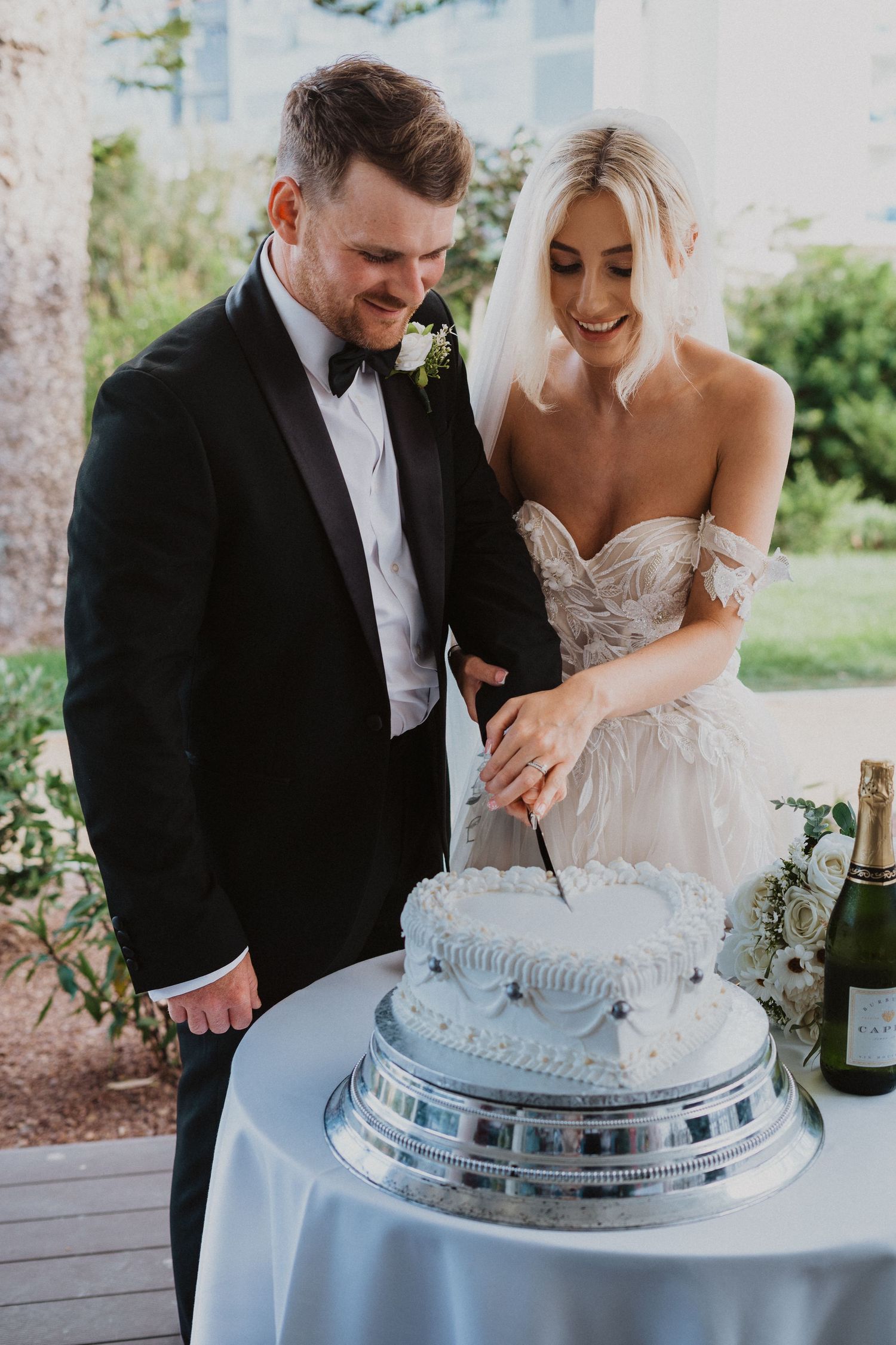 Newlyweds share intimate moment while cutting their wedding cake outdoors.