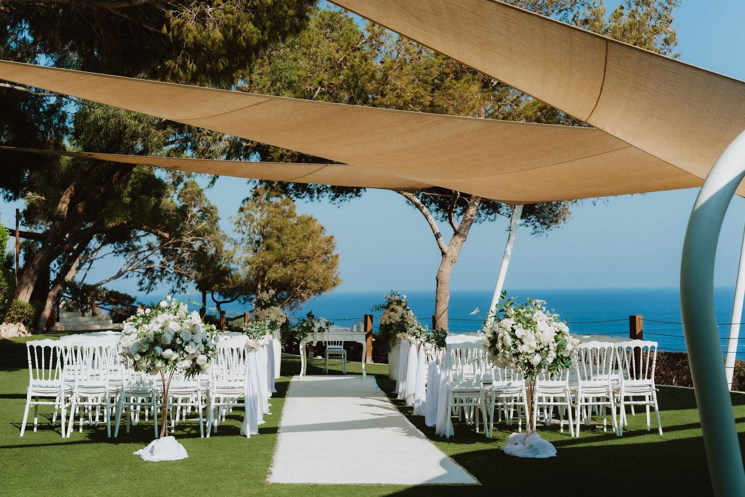Elegant outdoor wedding ceremony setup with white chairs and fabric canopy overlooking a blue ocean vista.