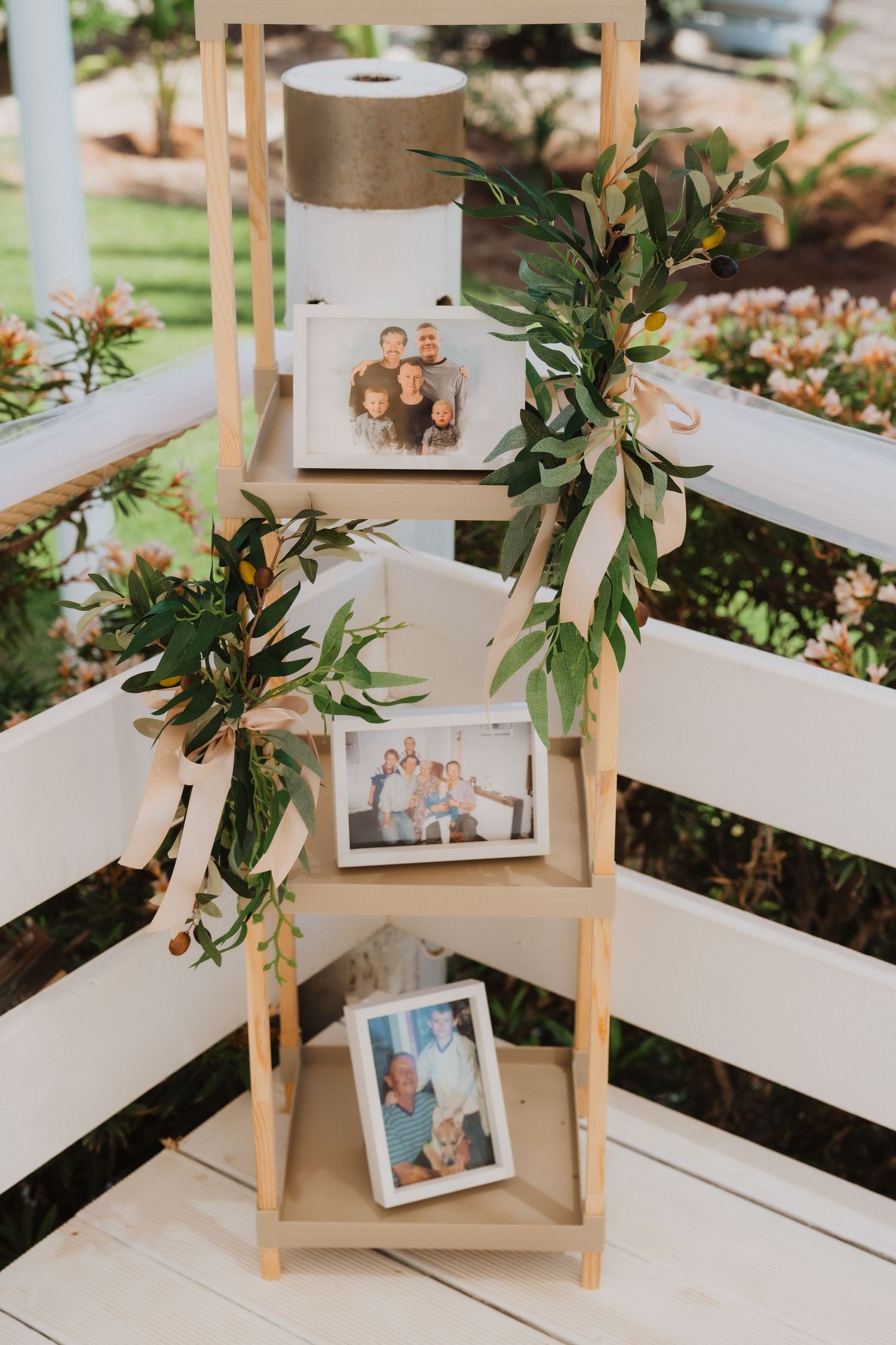 Wooden ladder shelf decorated with greenery and vintage photographs at a wedding reception setup.