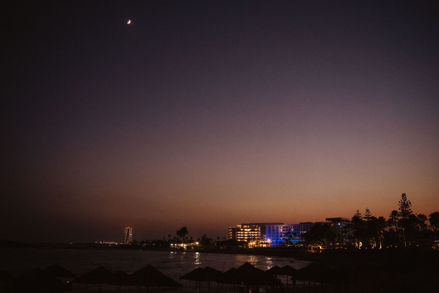 Coastal cityscape at dusk with buildings lit up against a purple sky.