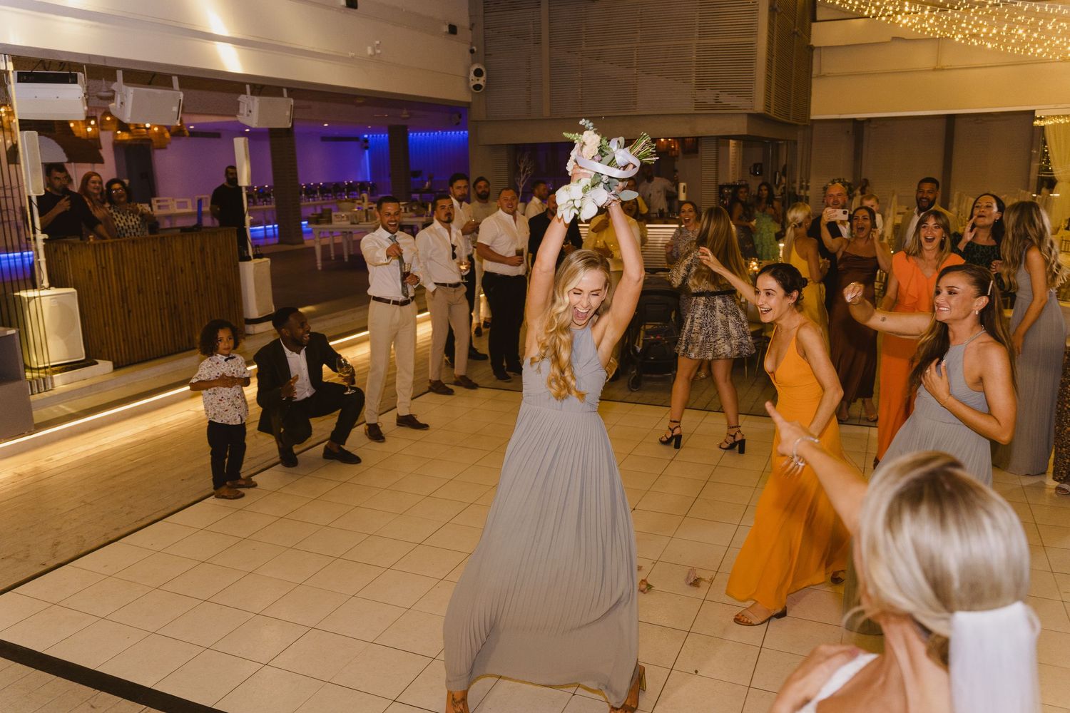 Wedding guests gather on the dance floor during the bouquet toss tradition.