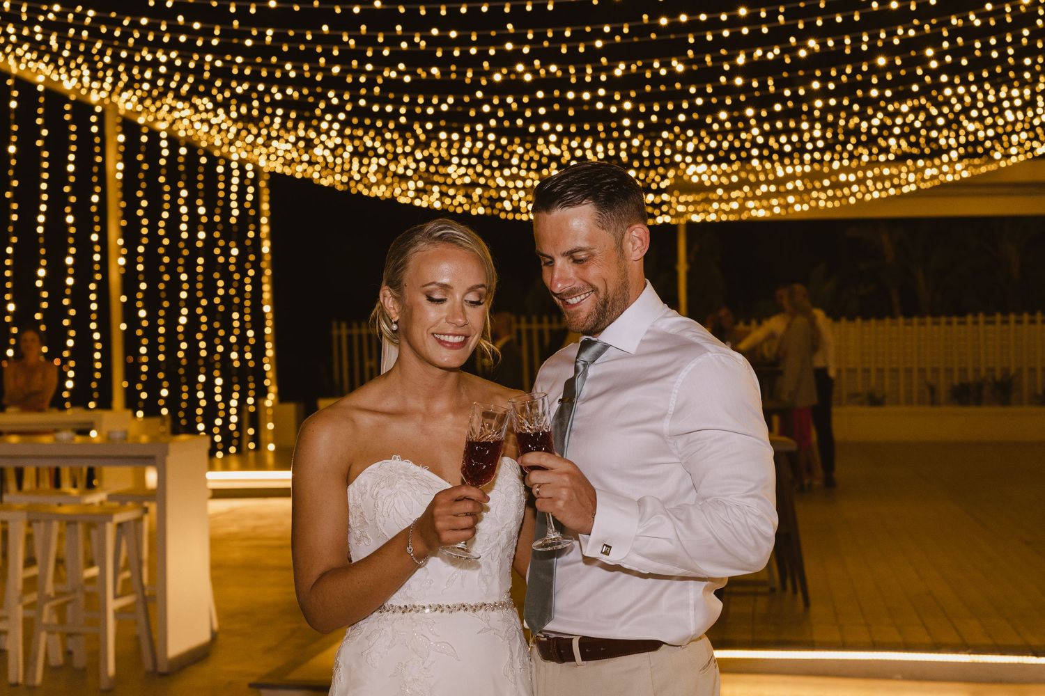 Couple shares an intimate moment with champagne under a ceiling of glowing fairy lights.