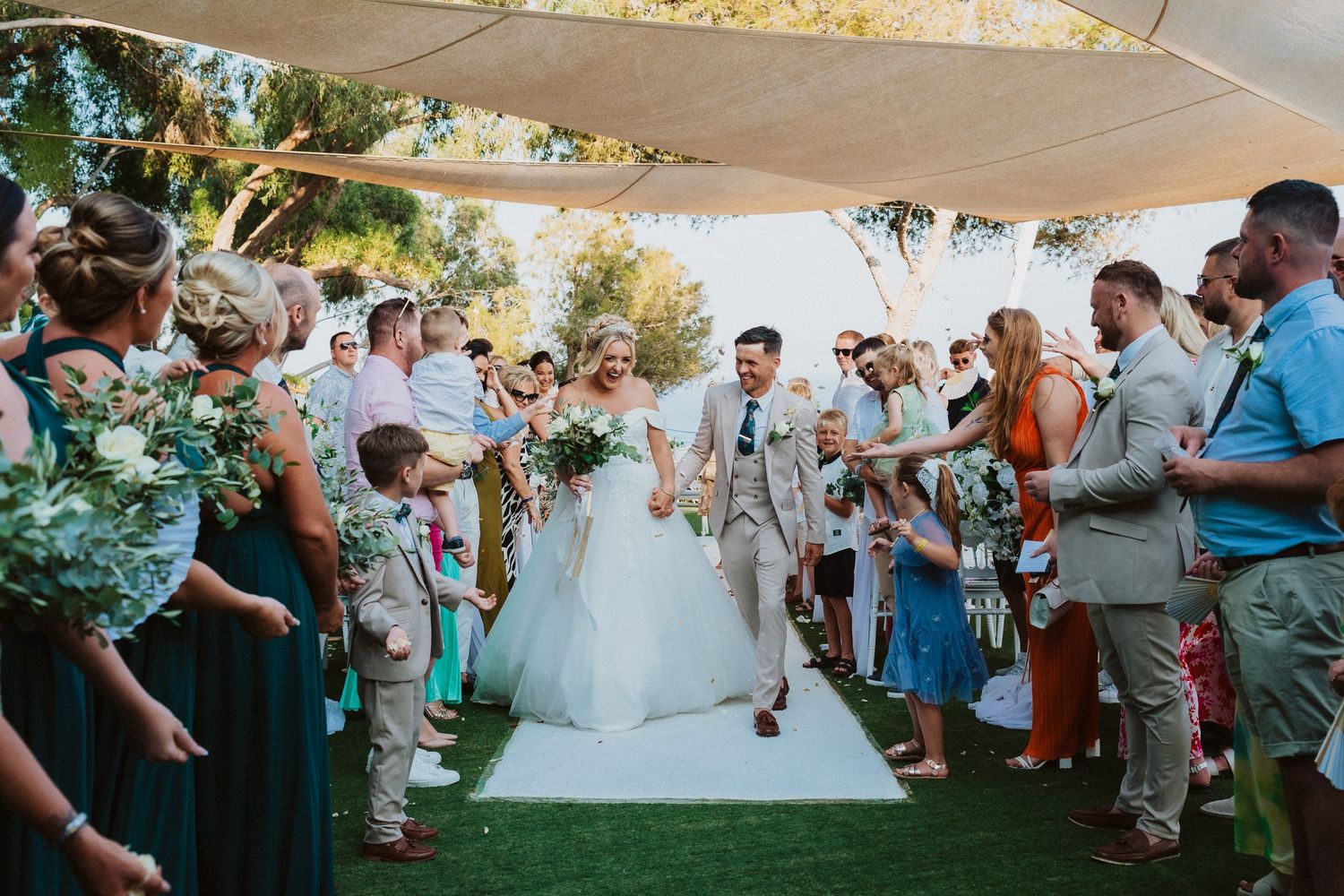 Guests cheer as newlyweds walk down the aisle at an outdoor wedding ceremony.