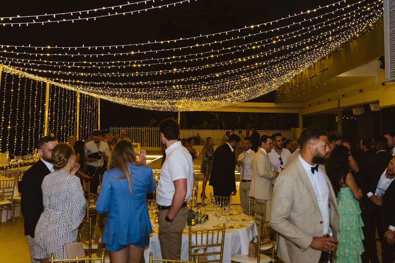 Wedding reception under canopy of twinkling string lights with guests mingling.