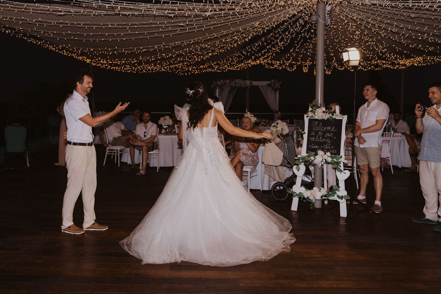 A flowing wedding dress twirls during a dance at an outdoor reception under fairy lights.