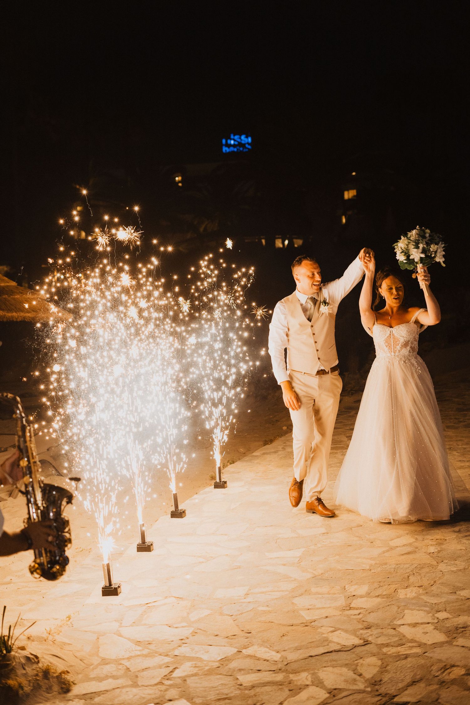 A romantic wedding dance moment at night with sparklers creating a magical pathway of light on a stone patio.