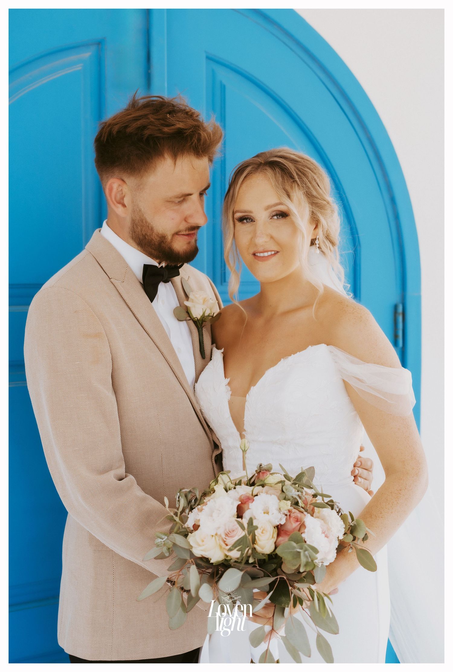 Wedding portrait featuring couple against bright blue door with elegant floral bouquet.