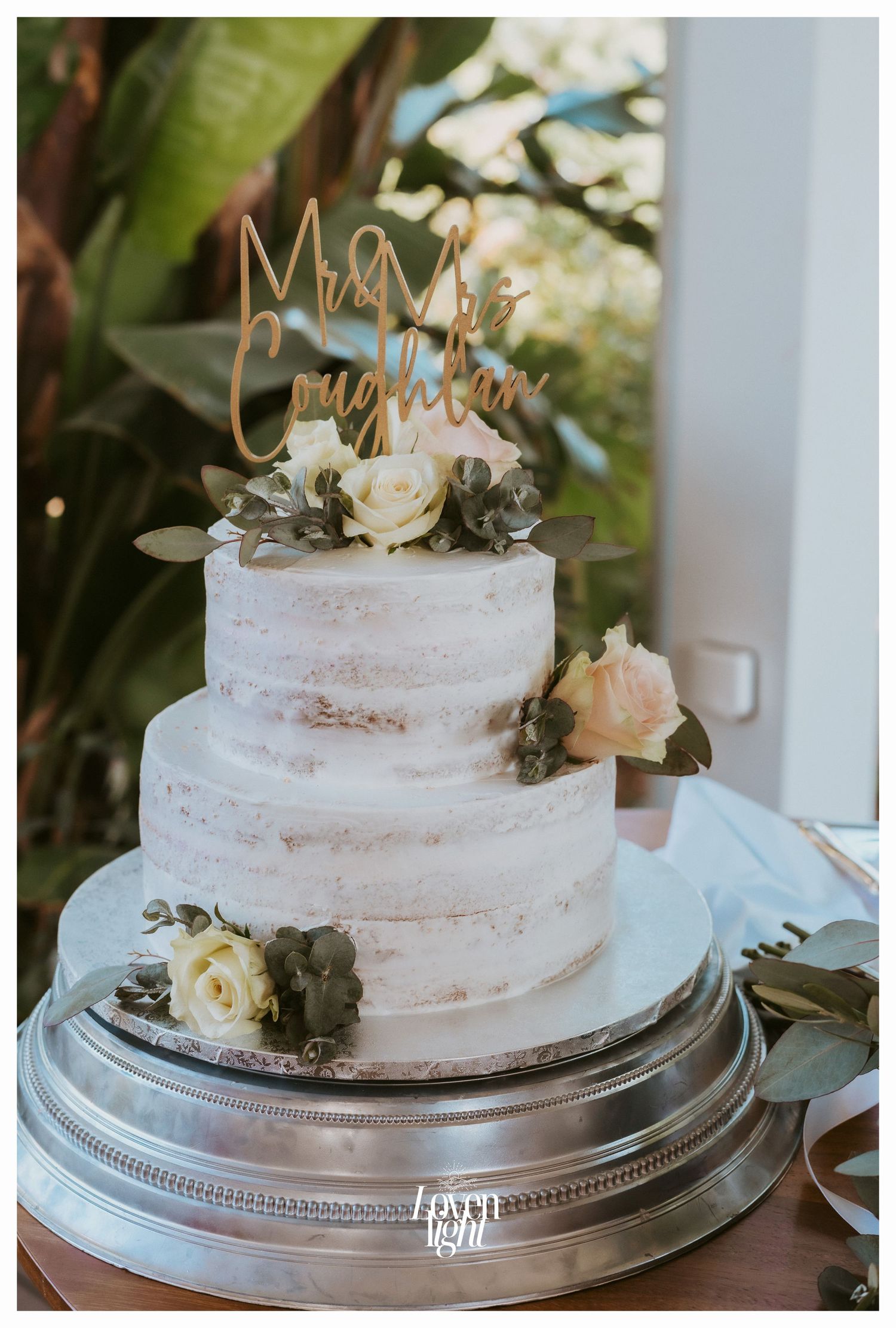 Three-tier semi-naked wedding cake decorated with white roses and 