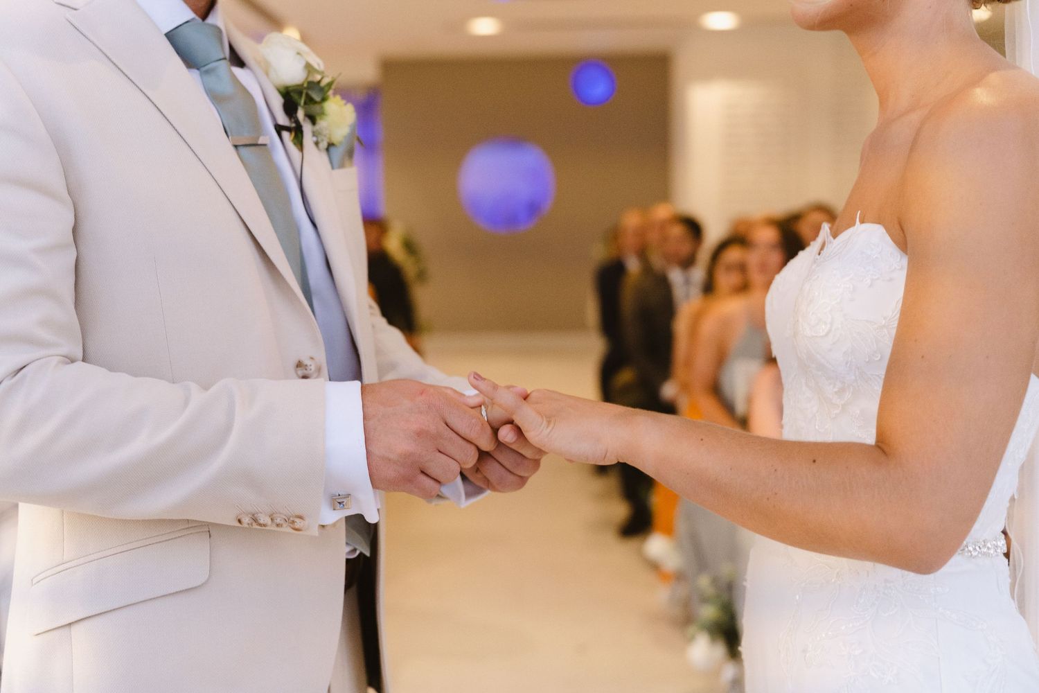 Close-up of a ring exchange during a wedding ceremony with soft purple lighting in the background.