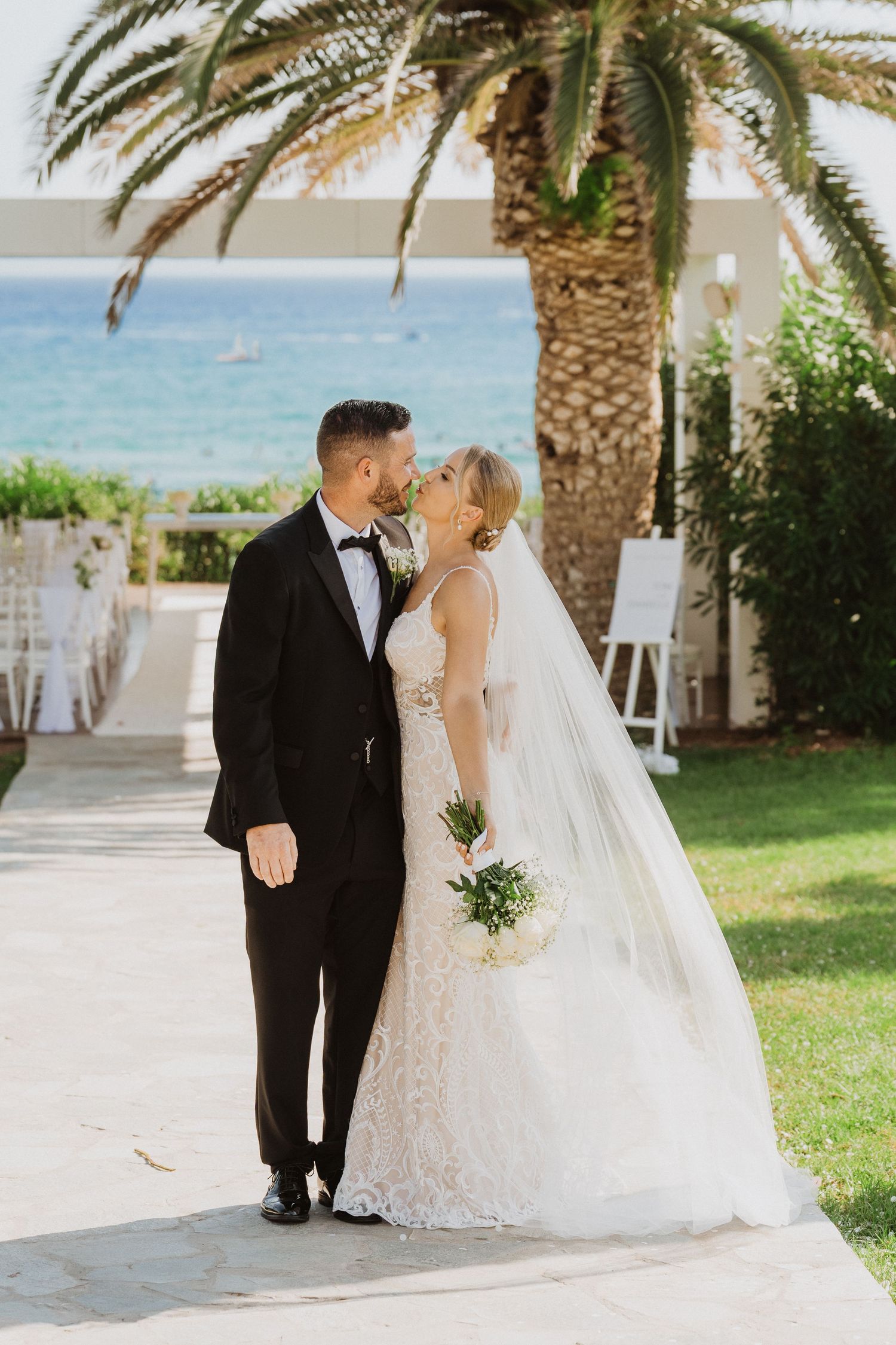 A romantic beach wedding couple poses under palm trees on a sunny day by the ocean.