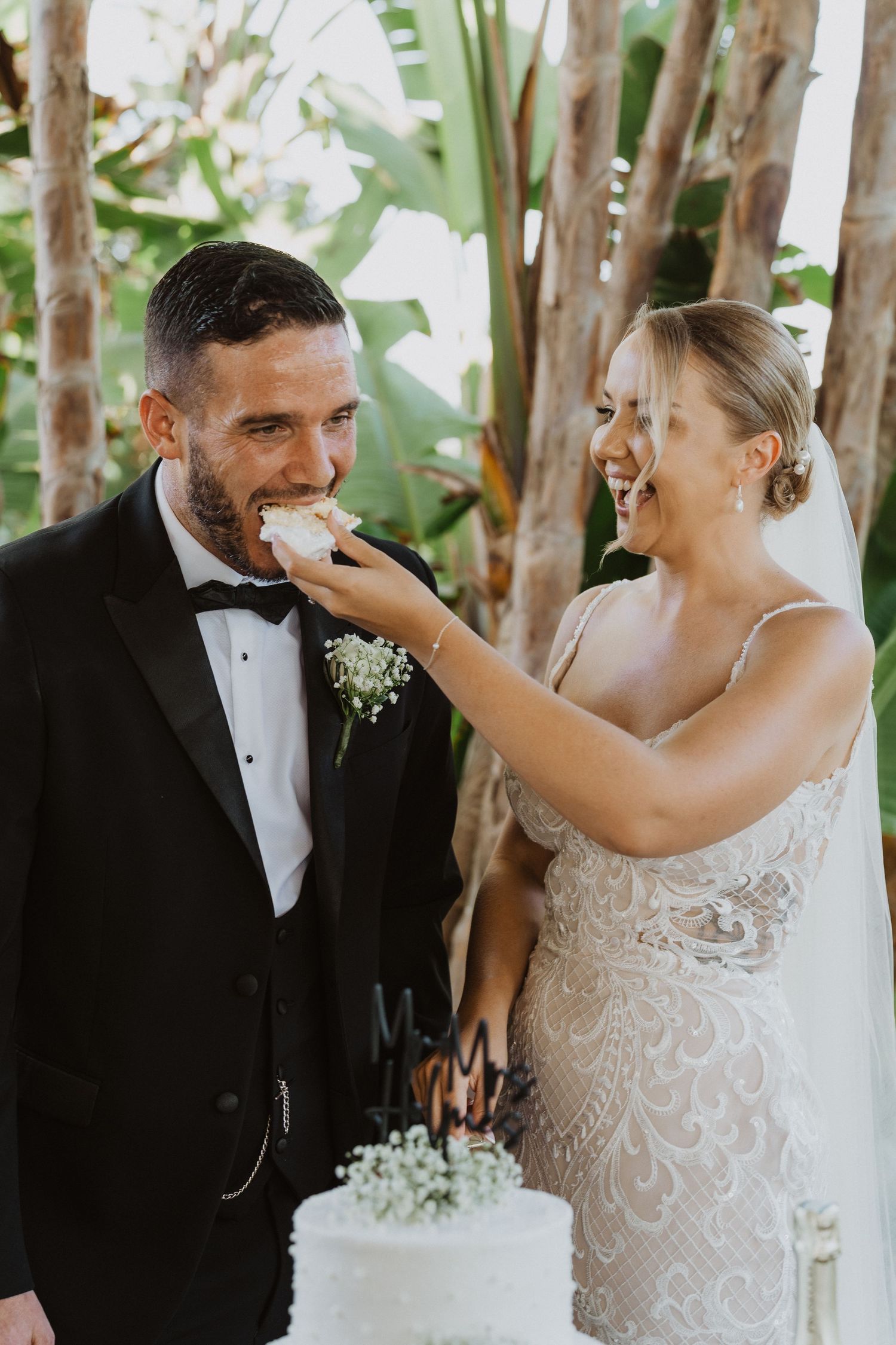 A joyful moment at a wedding as couple shares cake during their outdoor garden reception.