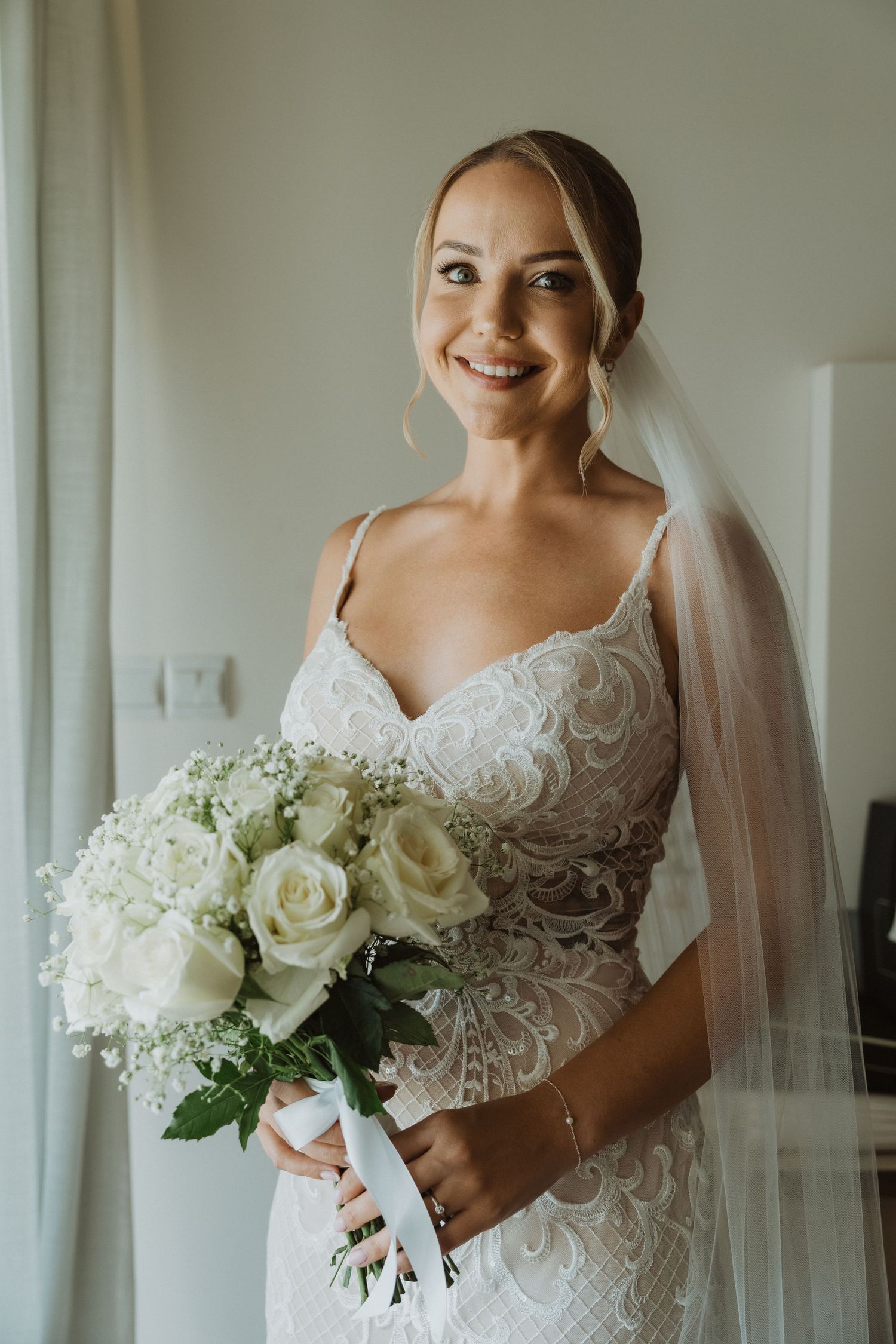 Elegant bride in white lace wedding dress holding classic white rose and hydrangea bouquet.