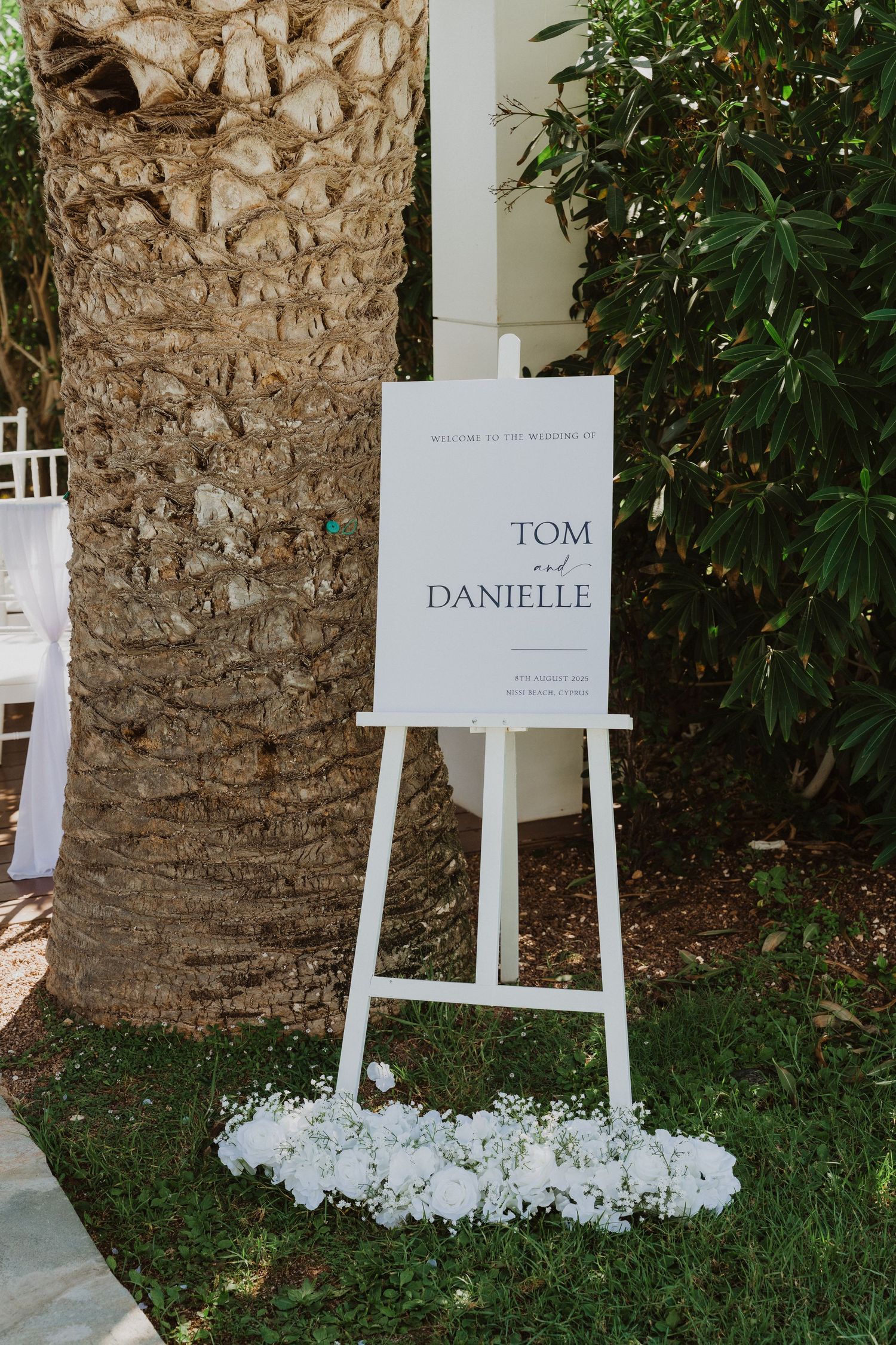 Wedding seating chart displays on white easels against a rustic stone wall with greenery.