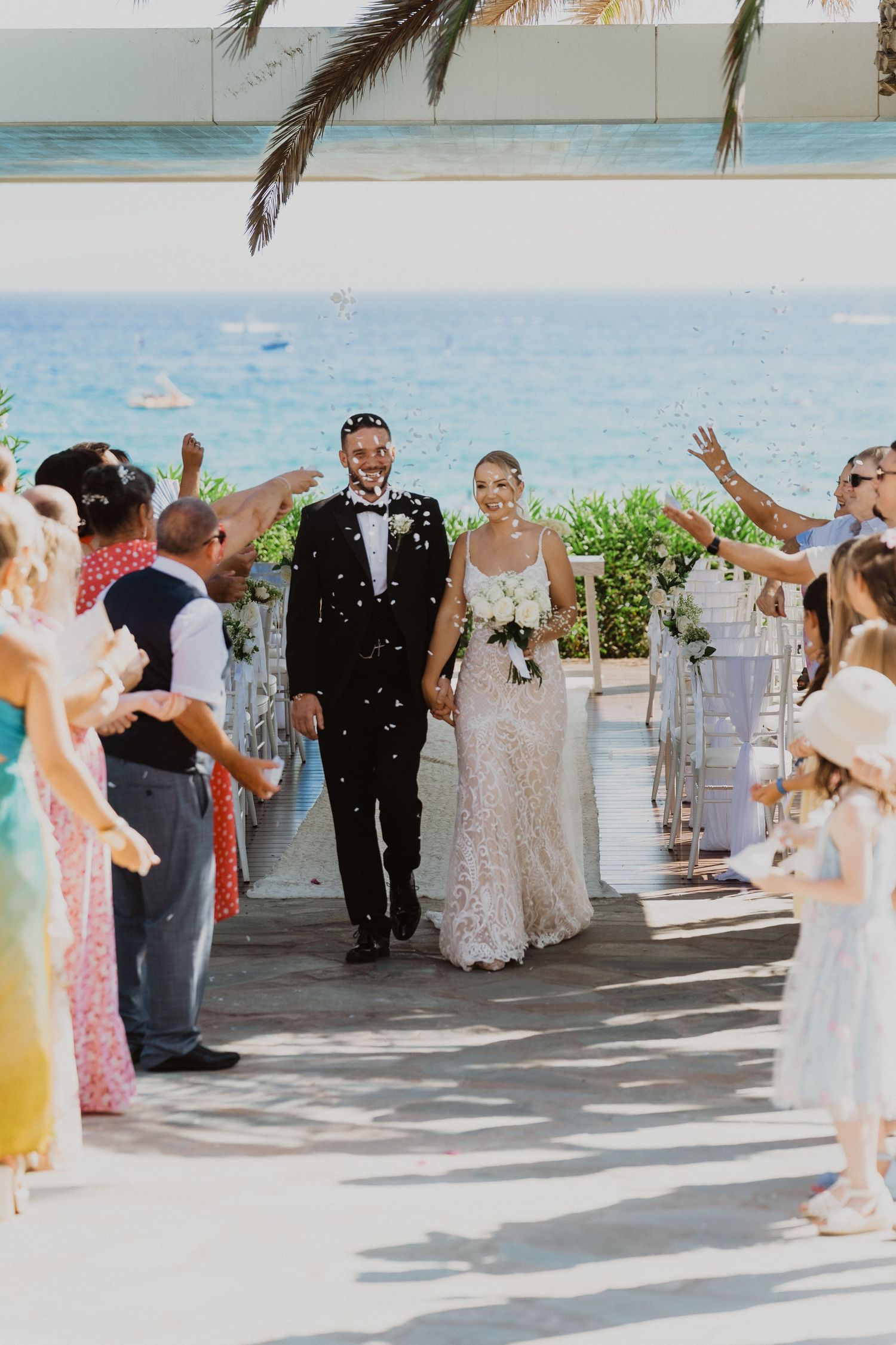 Wedding celebration at a beachside venue with guests throwing confetti under a covered walkway.