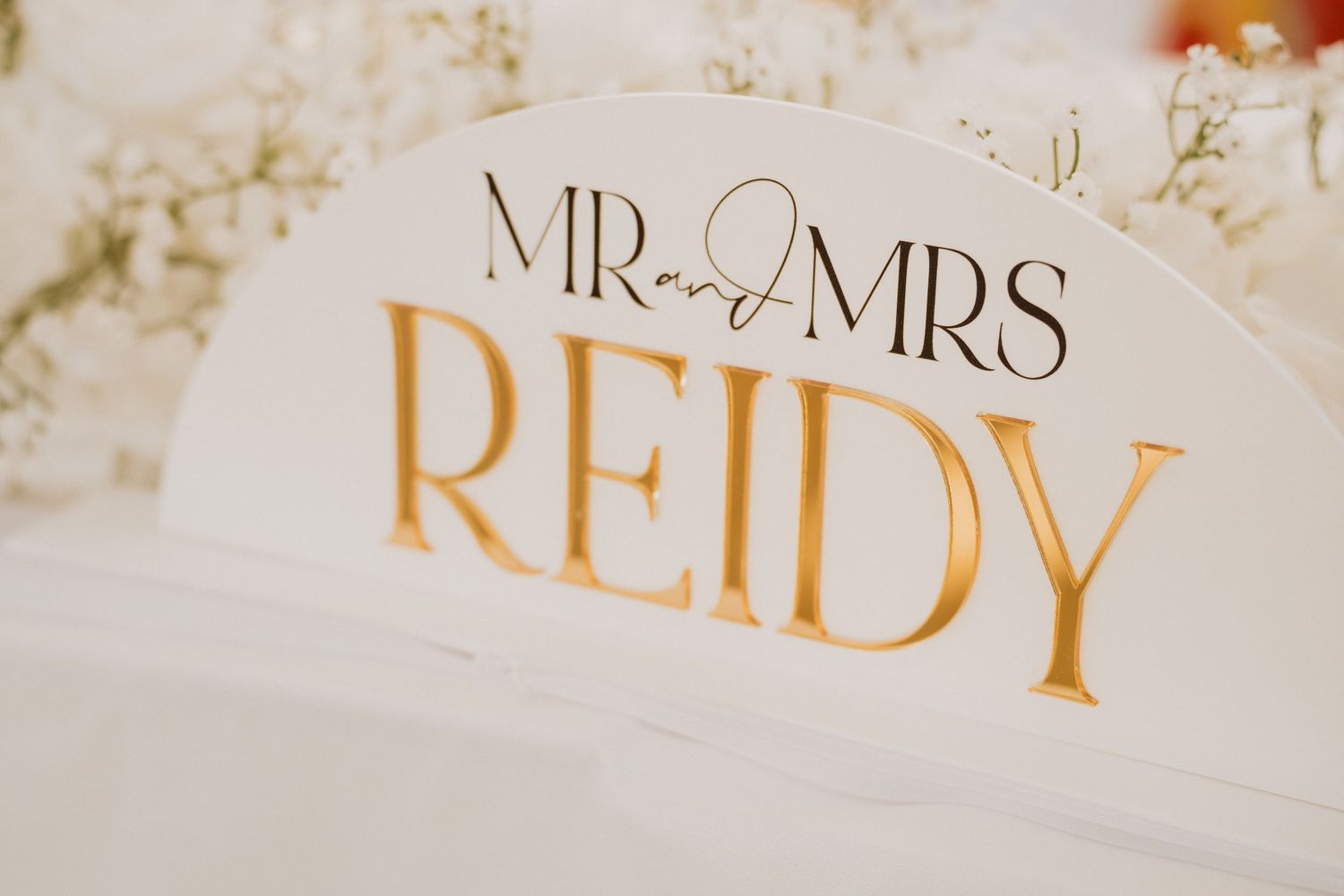 Gold and white Mr and Mrs Reidy wedding reception sign with ring detail on sweetheart table.