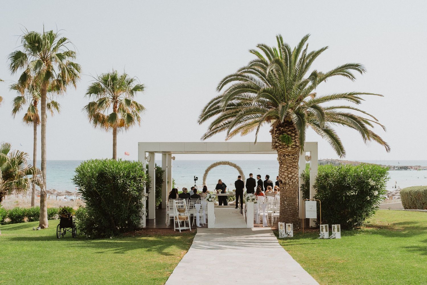 Elegant outdoor beach wedding ceremony setup with palm trees and white chairs.