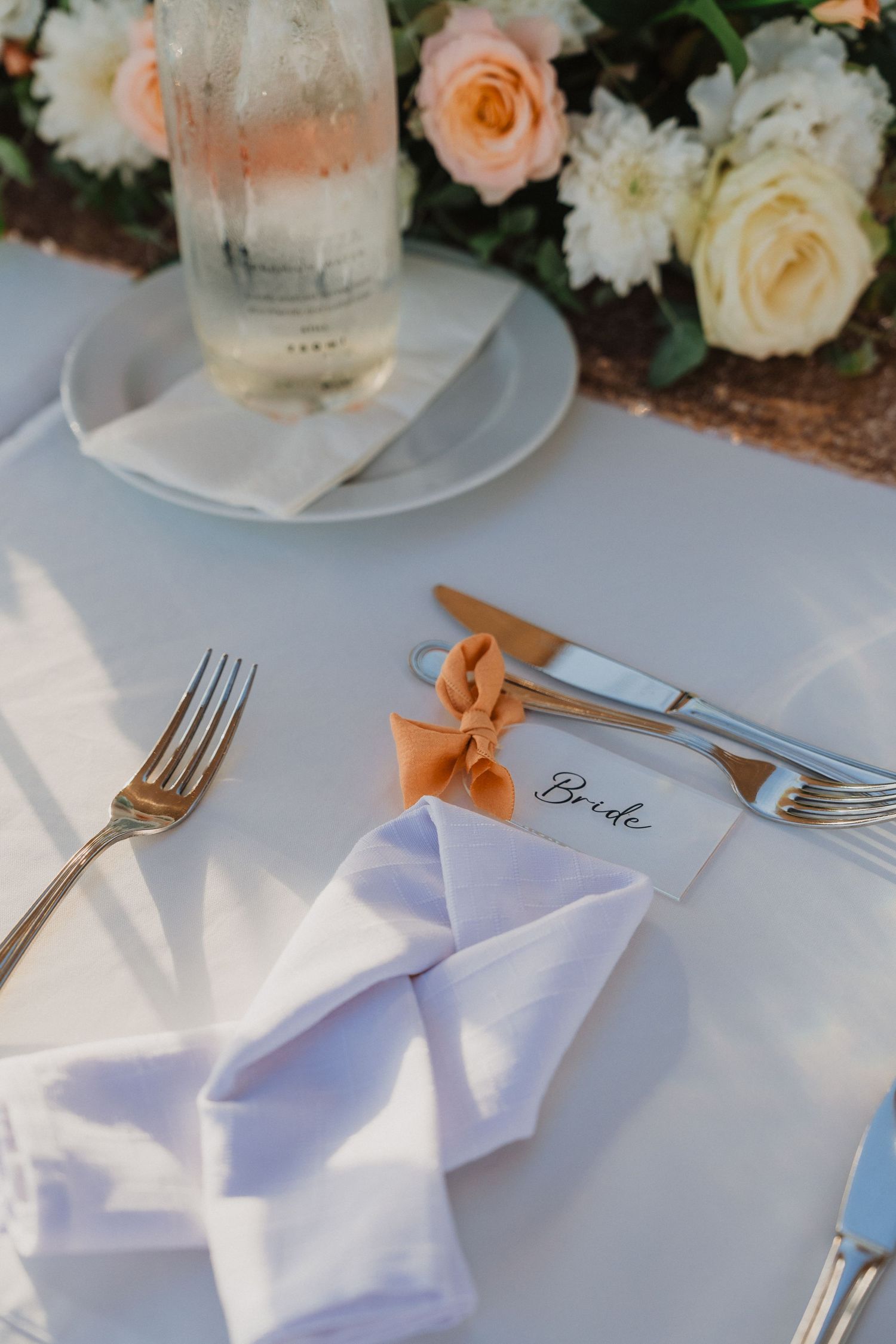 Elegant table setting with white napkin, roses, and place card for wedding reception.