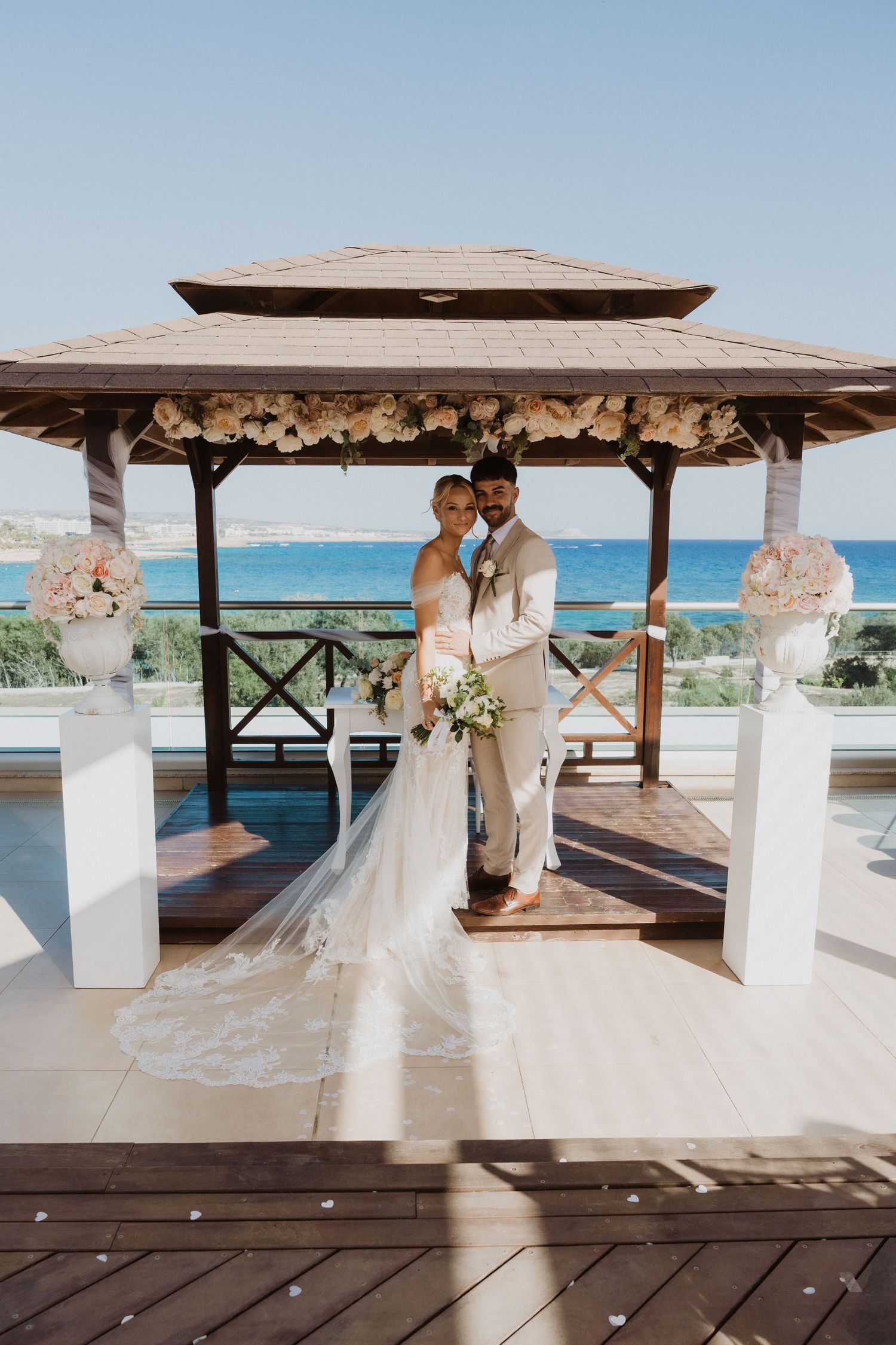 Wedding ceremony setup under a wooden pergola with ocean views and floral decorations.