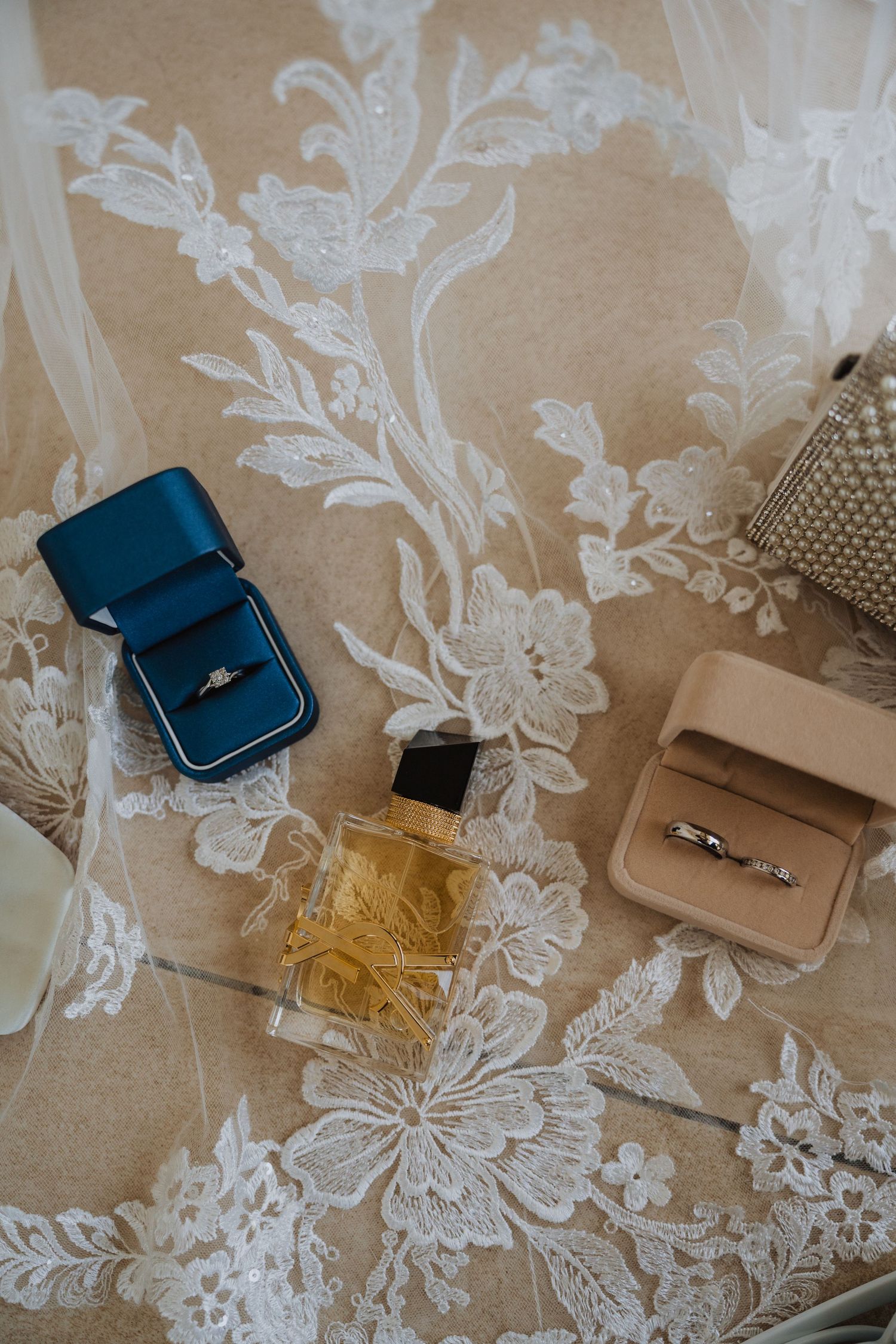 Wedding rings in blue velvet box with perfume bottle on lace fabric.