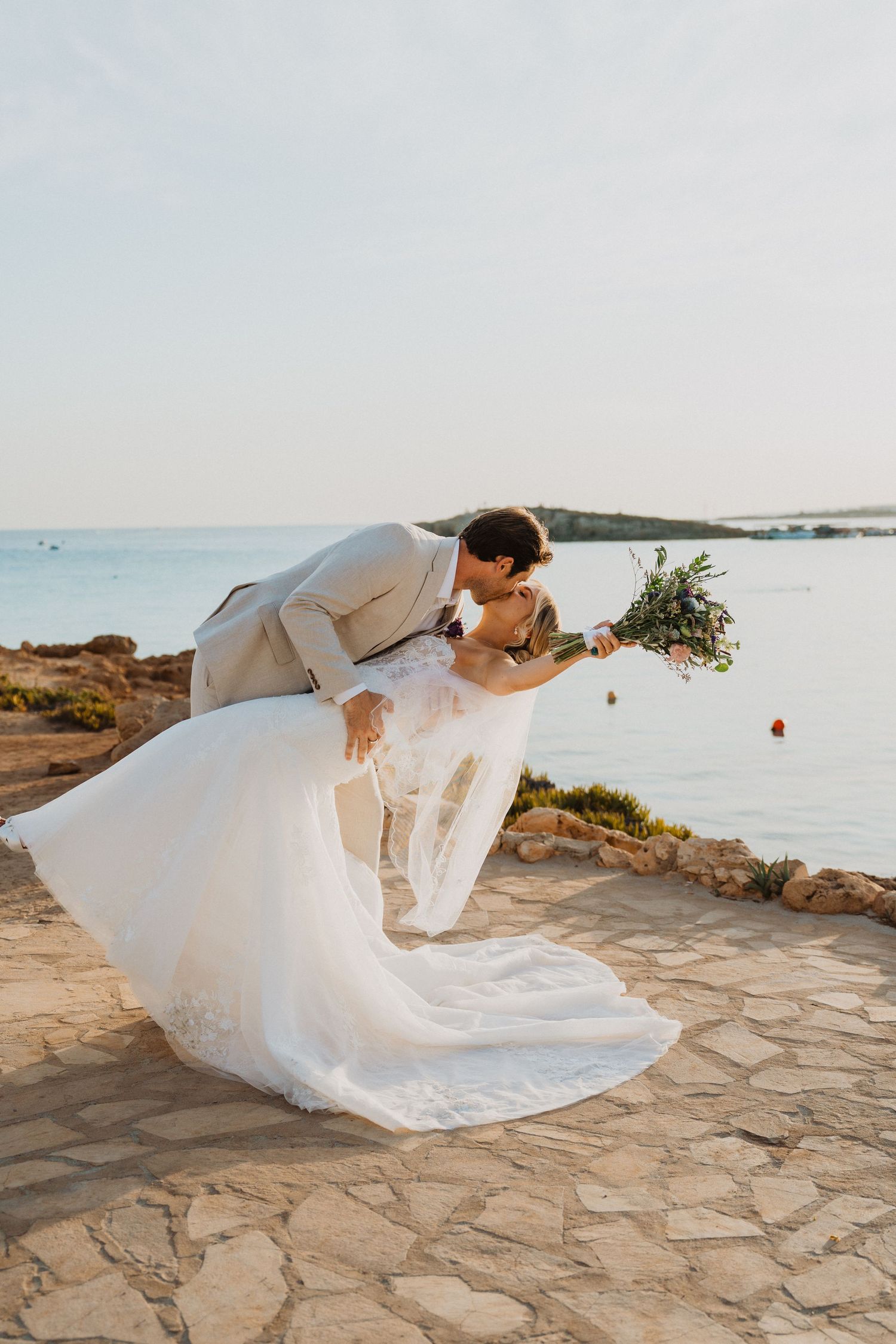 Flowing white wedding dress billowing in the wind against a coastal backdrop.