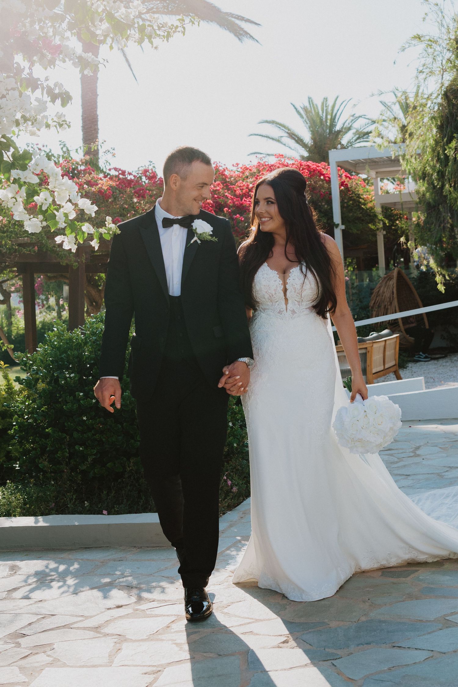 A couple dances together on a stone patio surrounded by palm trees and tropical flowers.