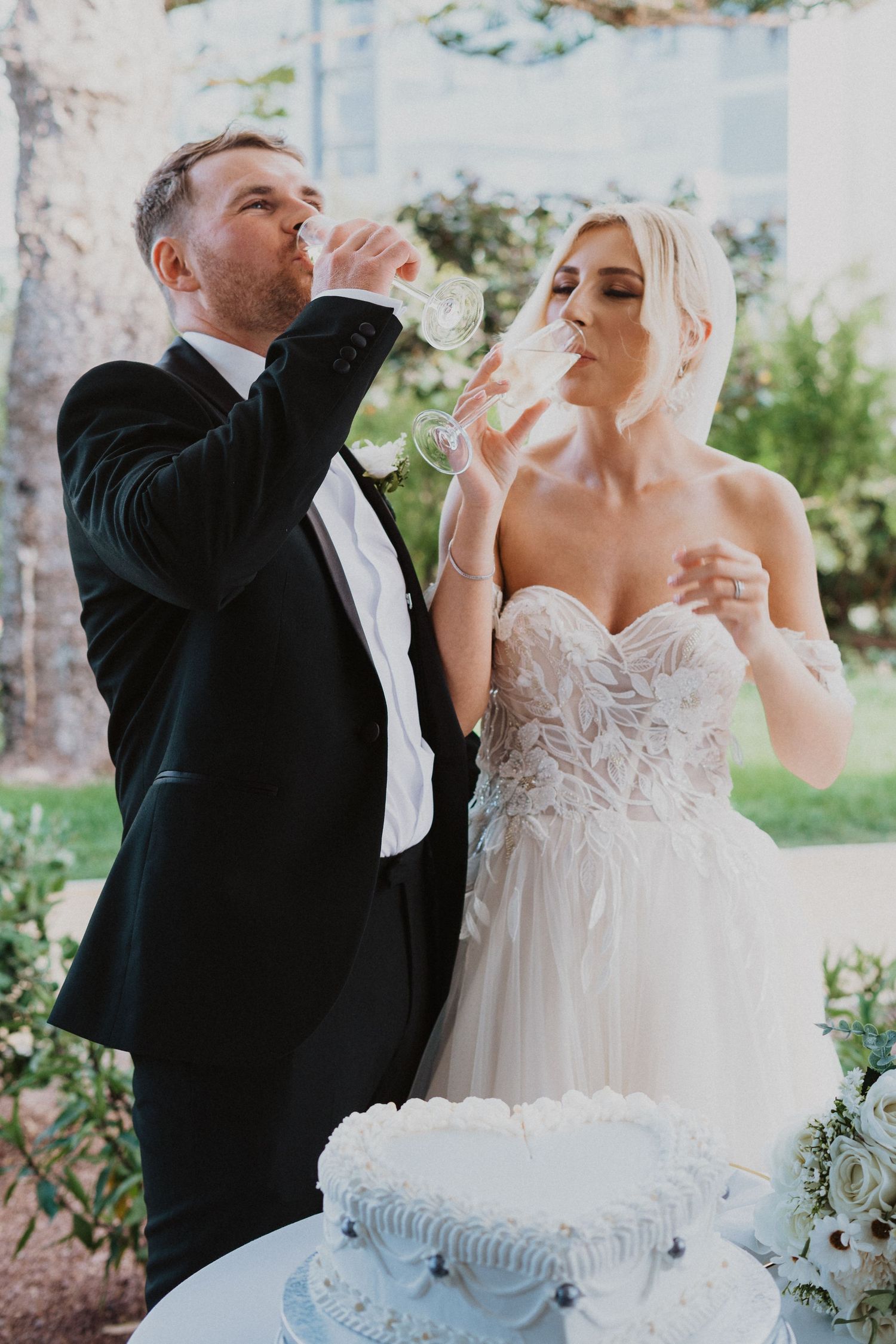 Wedding couple playfully tasting cake together during their reception in an outdoor garden setting.