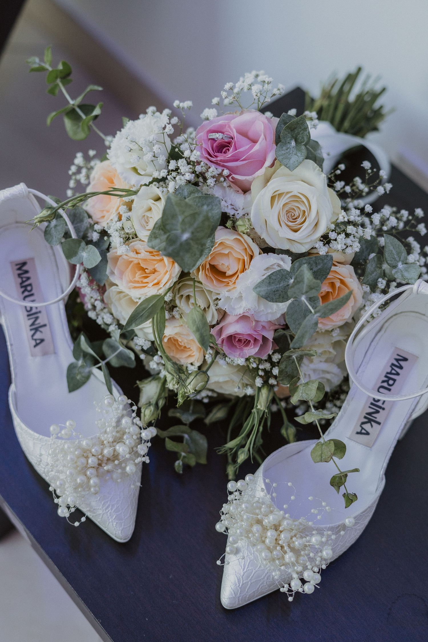 Elegant white bridal shoes displayed with a romantic rose and baby's breath bouquet.