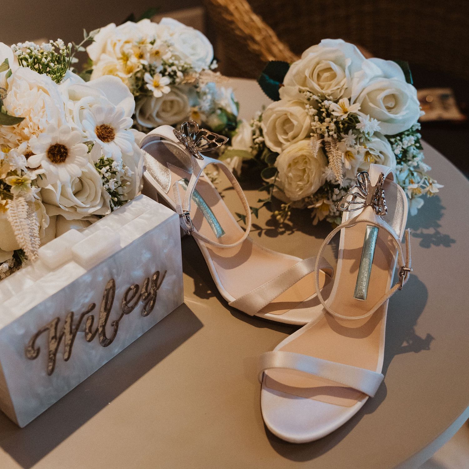 Wedding accessories including white rose bouquets and elegant strappy heels on display.