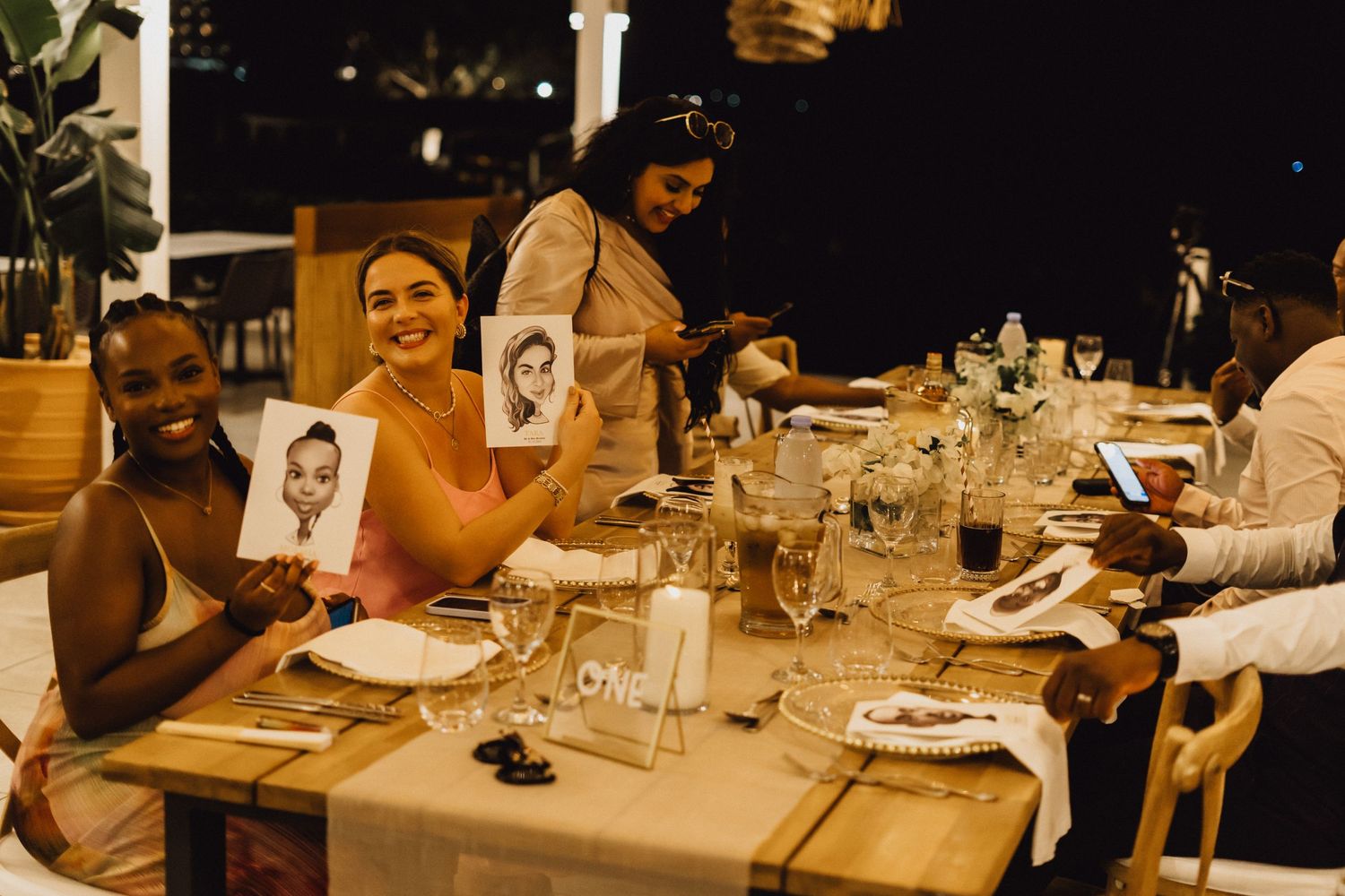 Wedding reception dinner table with guests enjoying drinks and conversation in warm lighting.