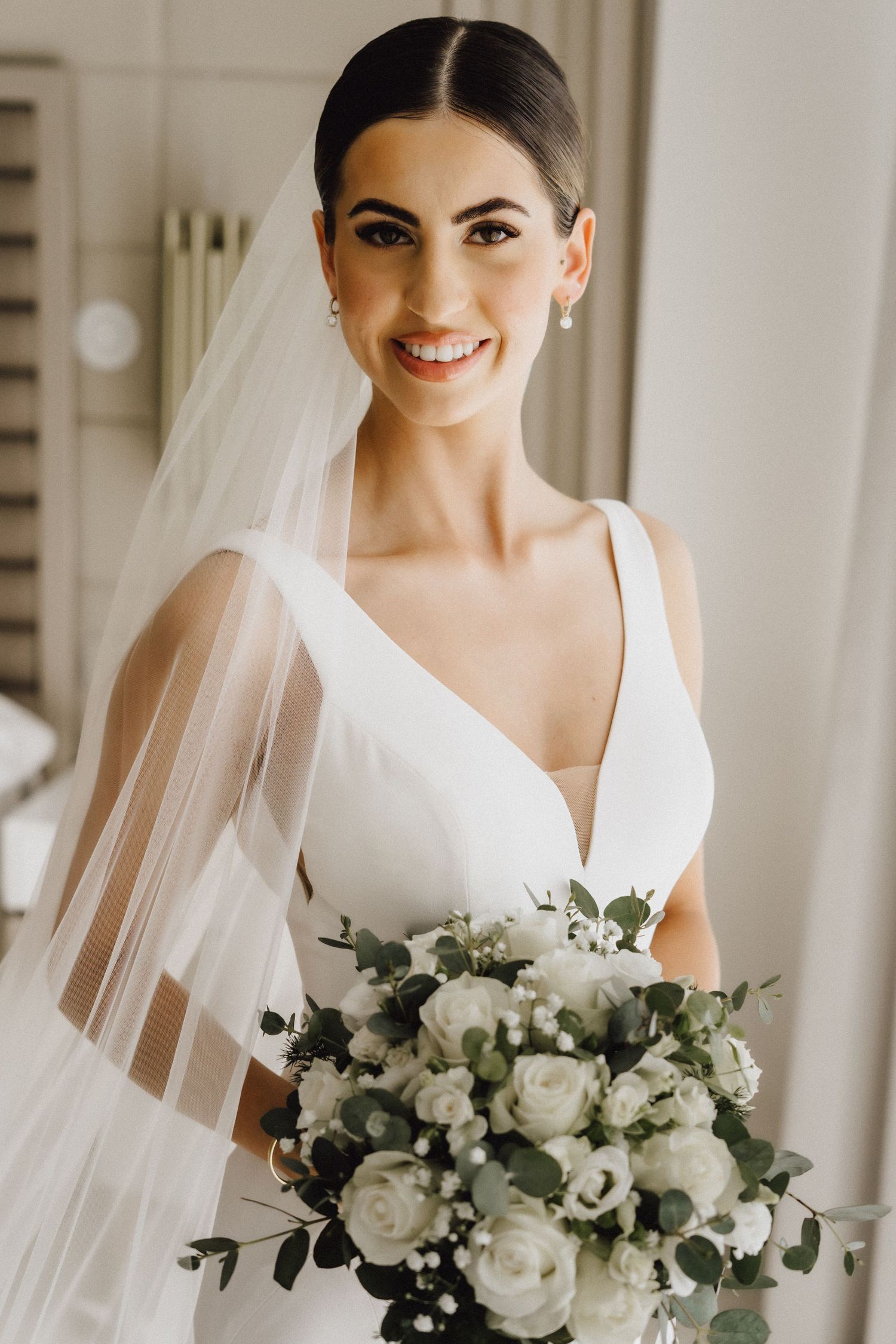 Elegant bride in minimalist white wedding dress holding romantic white and green bouquet.