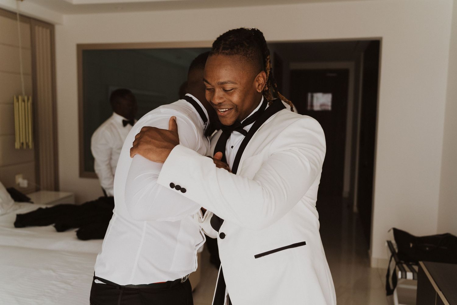Two people in white tuxedo jackets embrace while getting ready for a formal event.