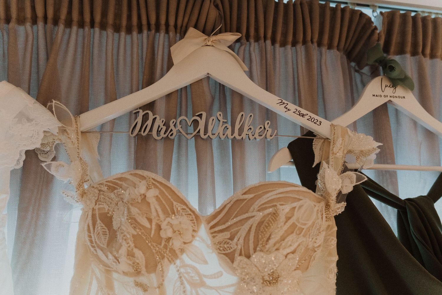 A white wedding dress on a personalized hanger displayed against curtains.