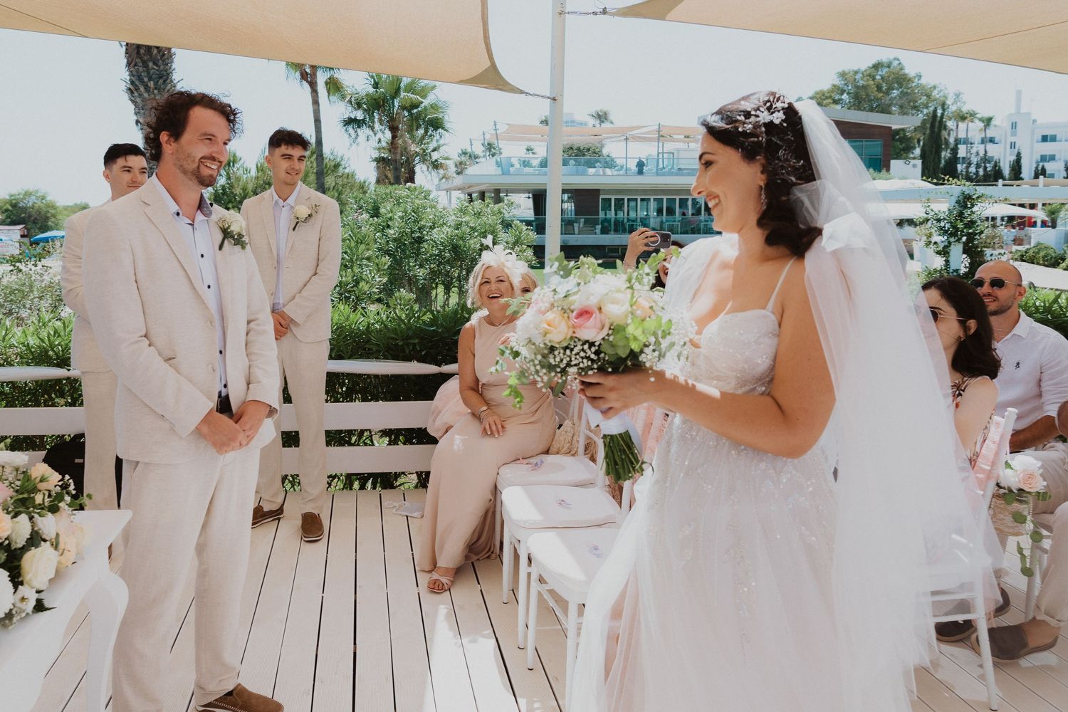 Beautiful outdoor wedding ceremony with light beige decor and floral arrangements on a deck.
