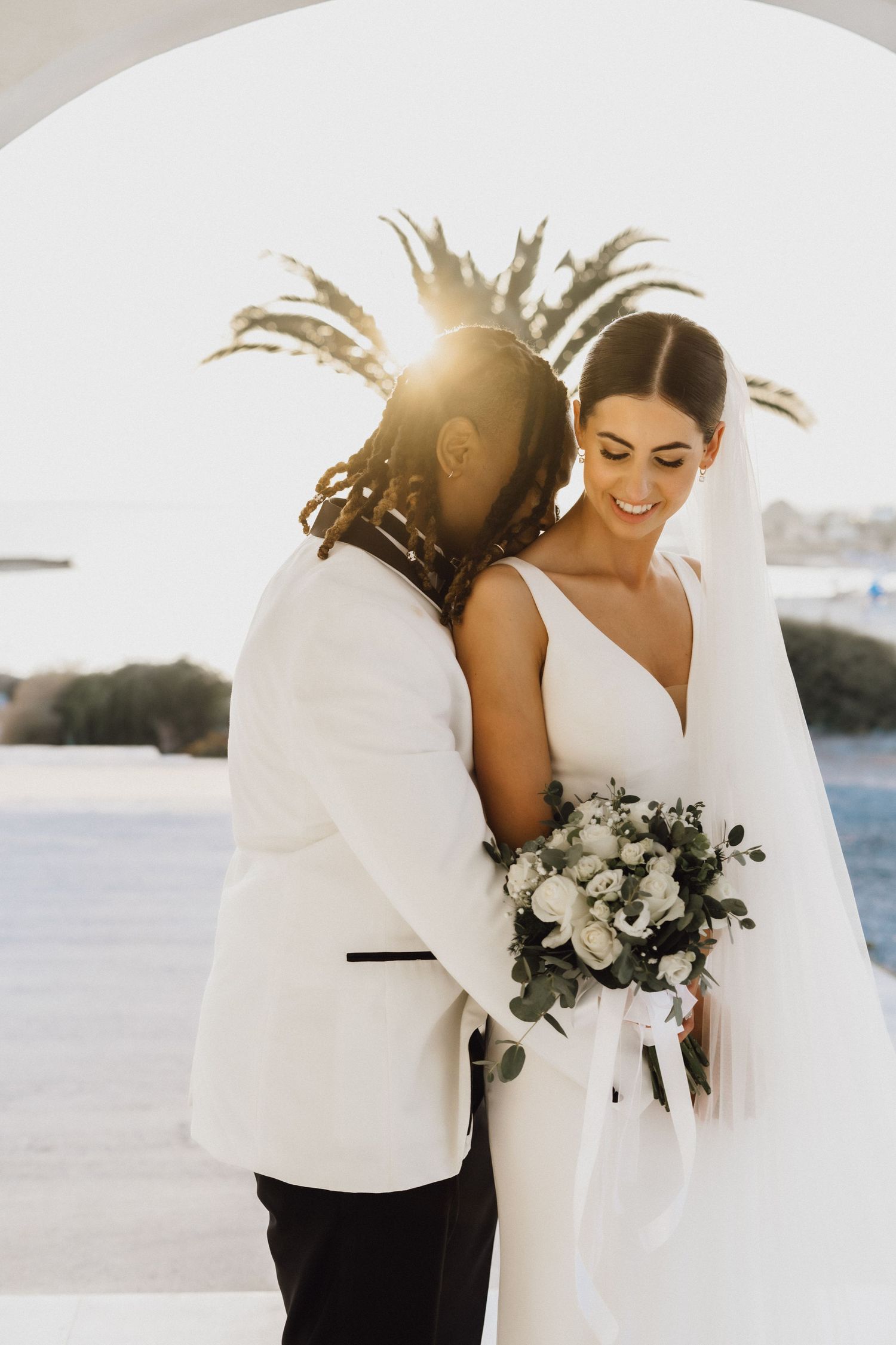 Sunlit wedding portrait under Mediterranean archway with white florals.