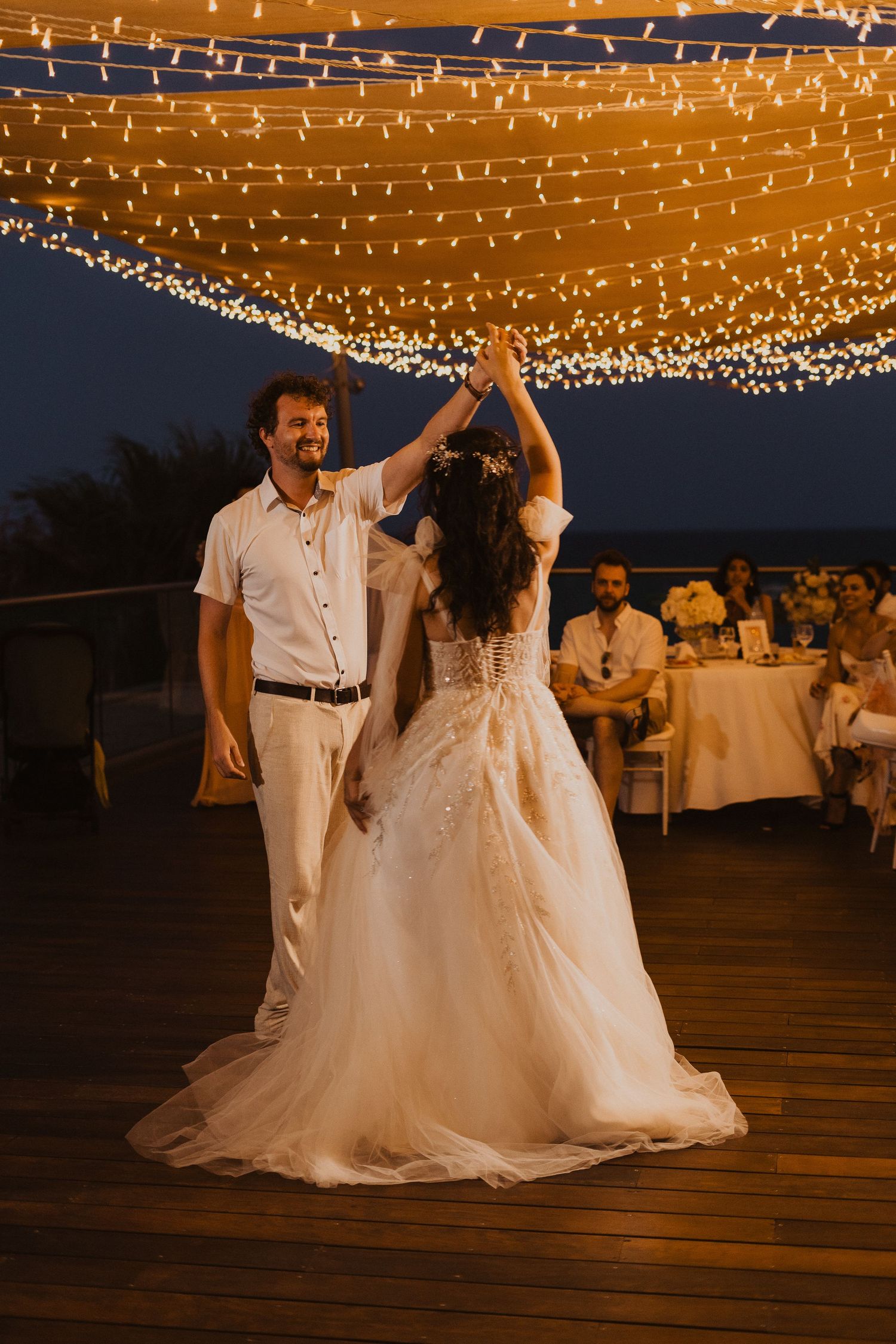 A dancing couple spins under golden string lights at their outdoor wedding reception.
