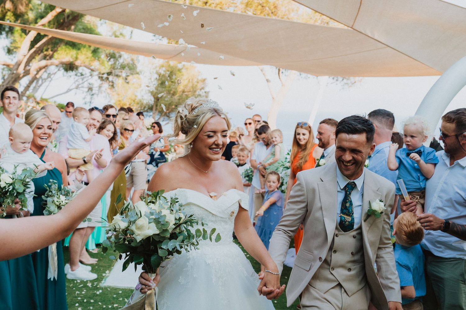 Joyful wedding celebration with guests cheering as couple walks through outdoor venue.
