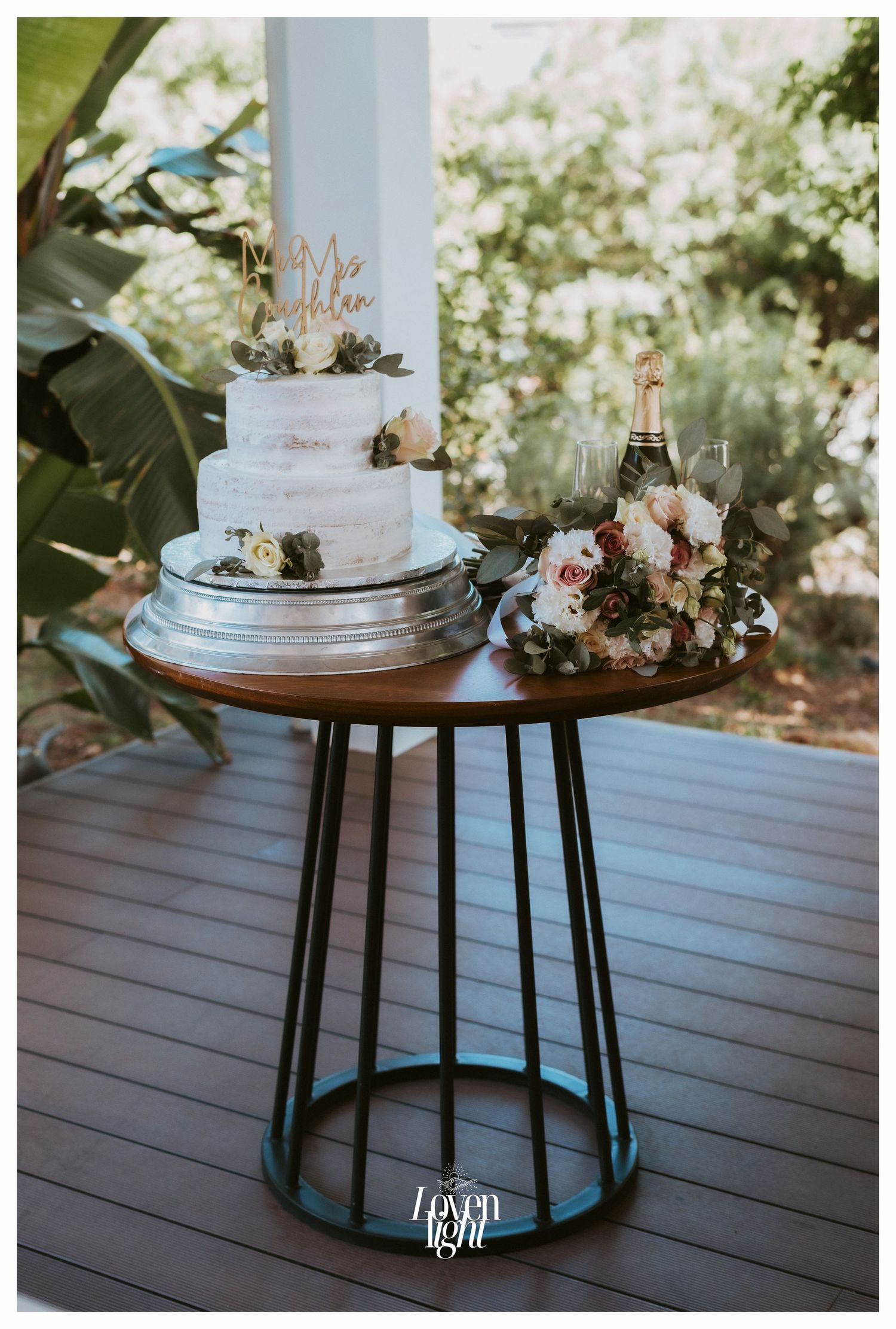 Wedding cake display on modern metal table with floral arrangements.