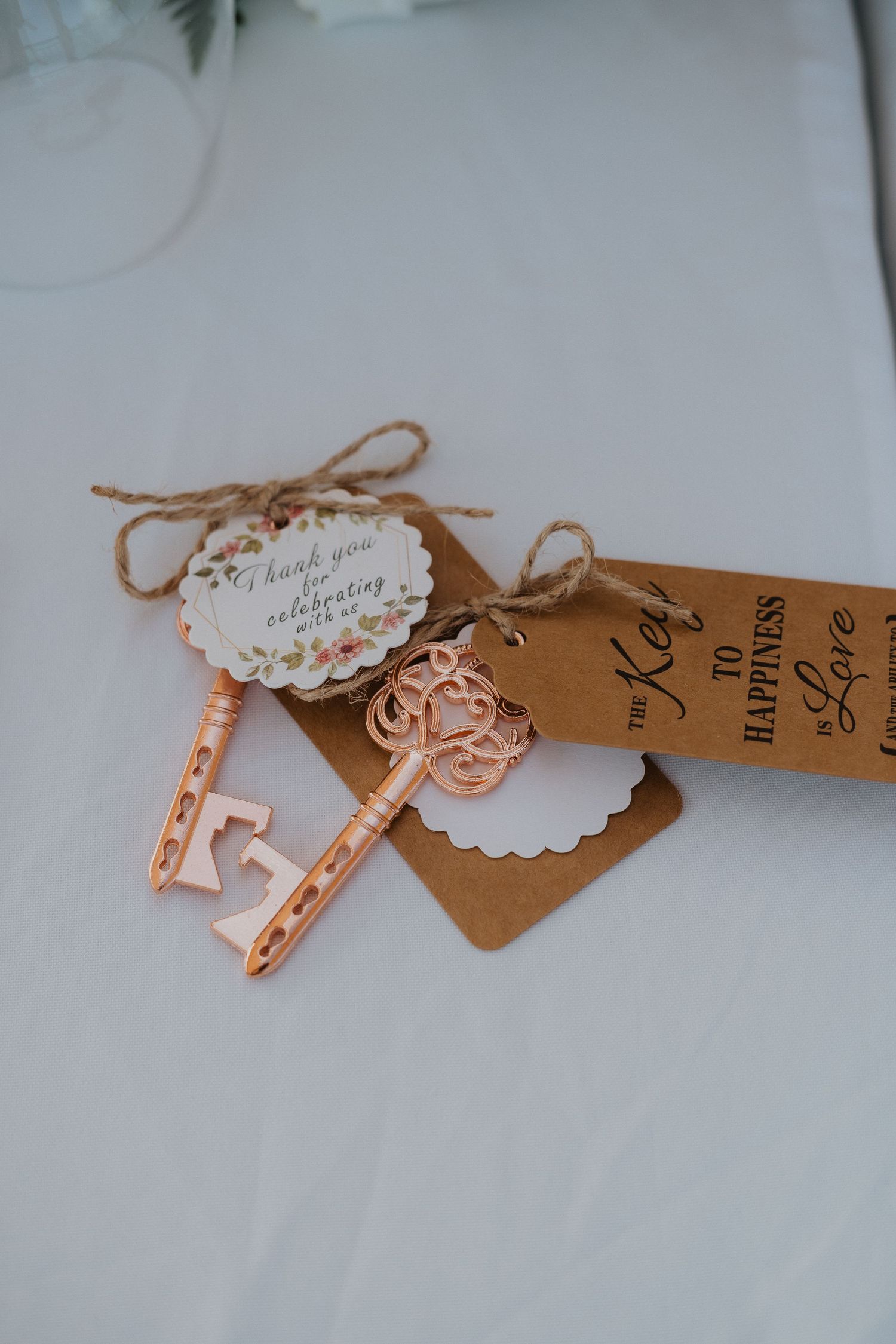 Decorative rose gold key and kraft paper tag with twine bow on white surface.