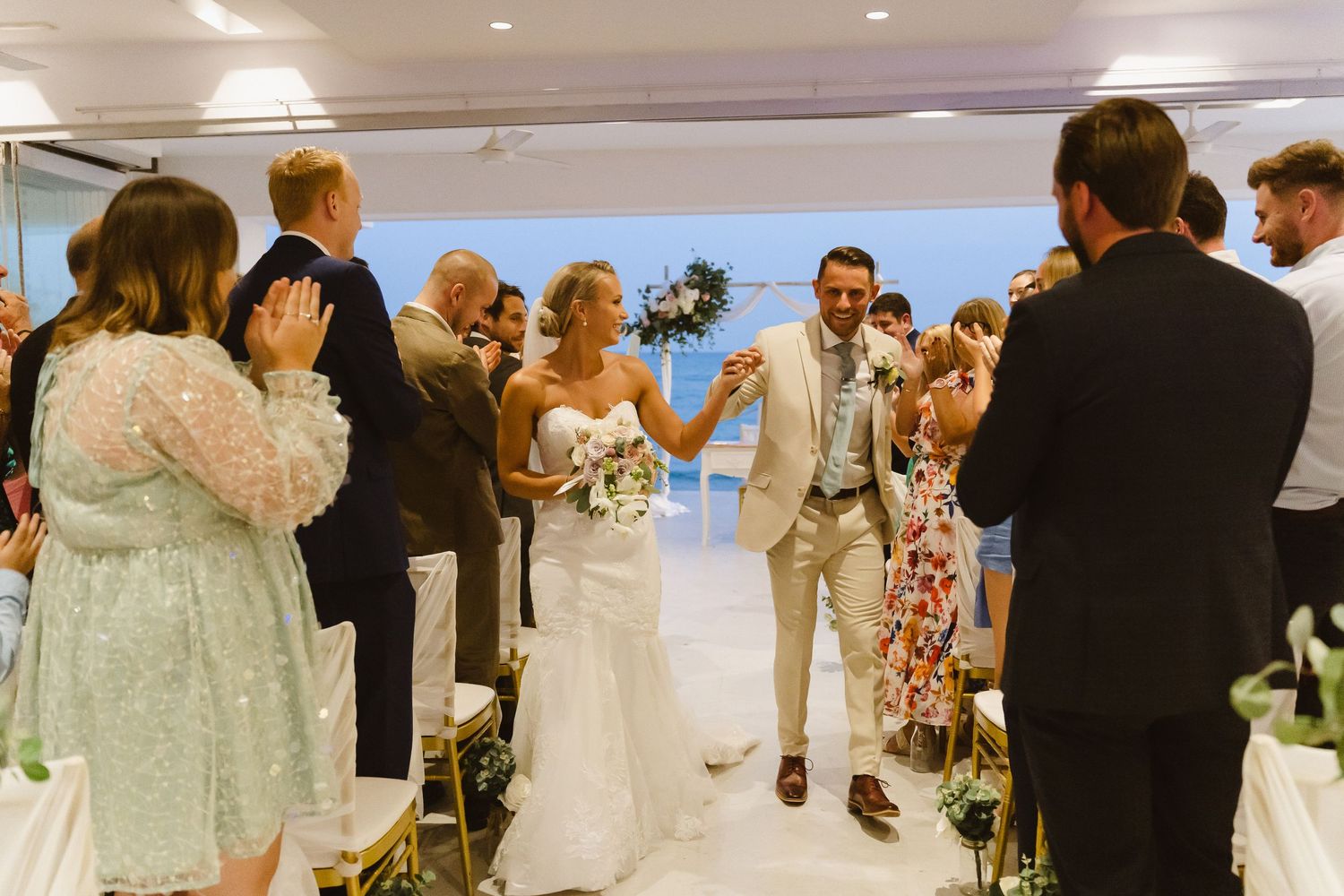 Joyful wedding recessional with guests clapping as couple walks down decorated aisle.