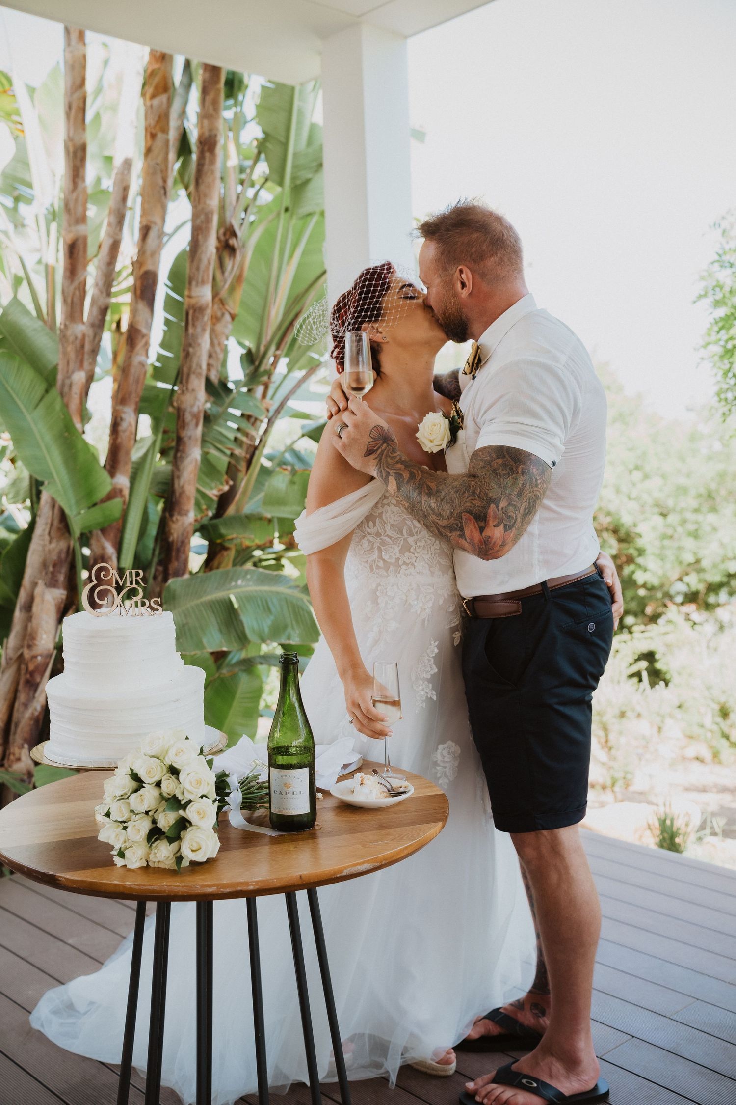Wedding couple embracing next to their cake table on outdoor patio.