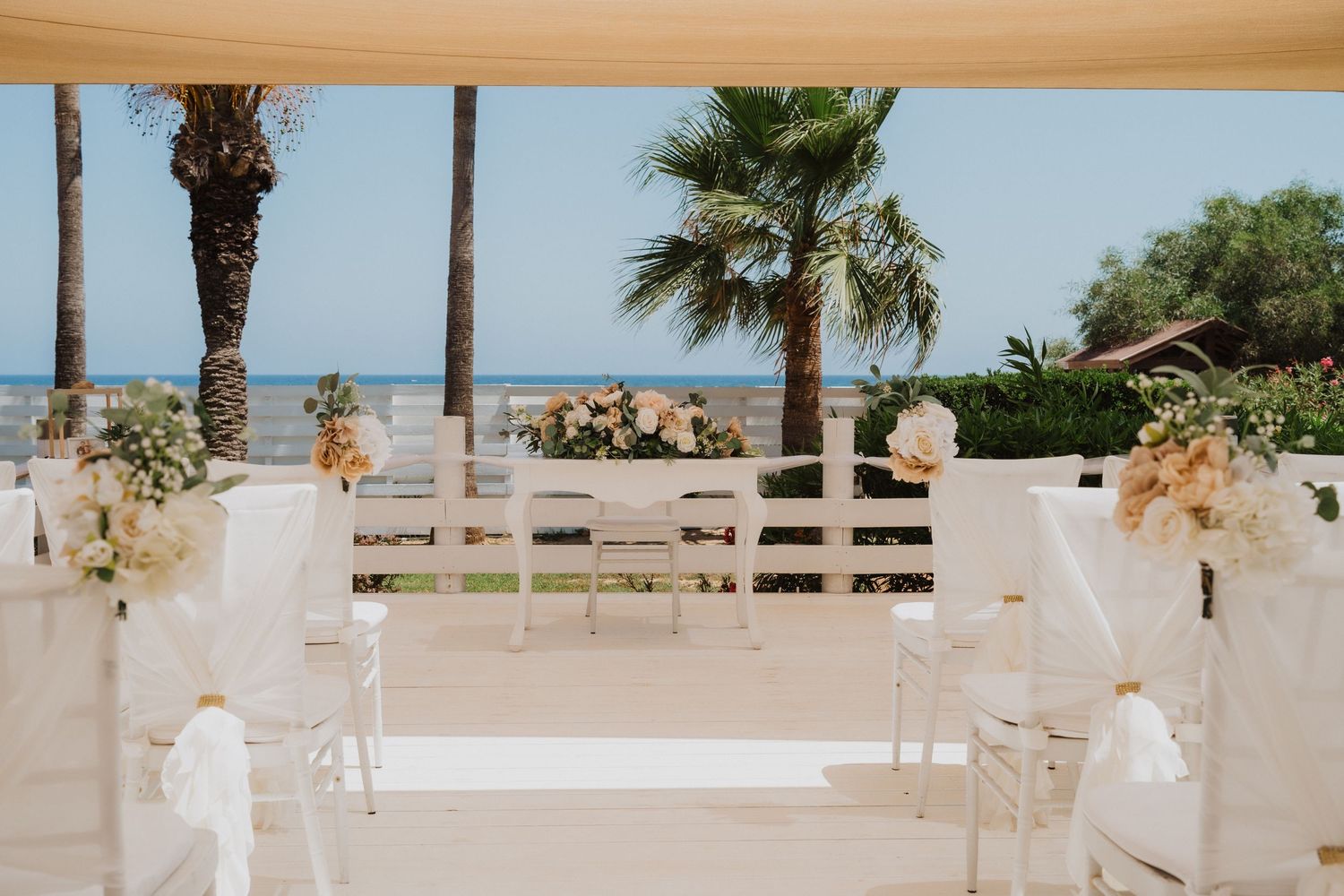 Beachside wedding ceremony setup with white benches and floral arrangements framing the aisle.