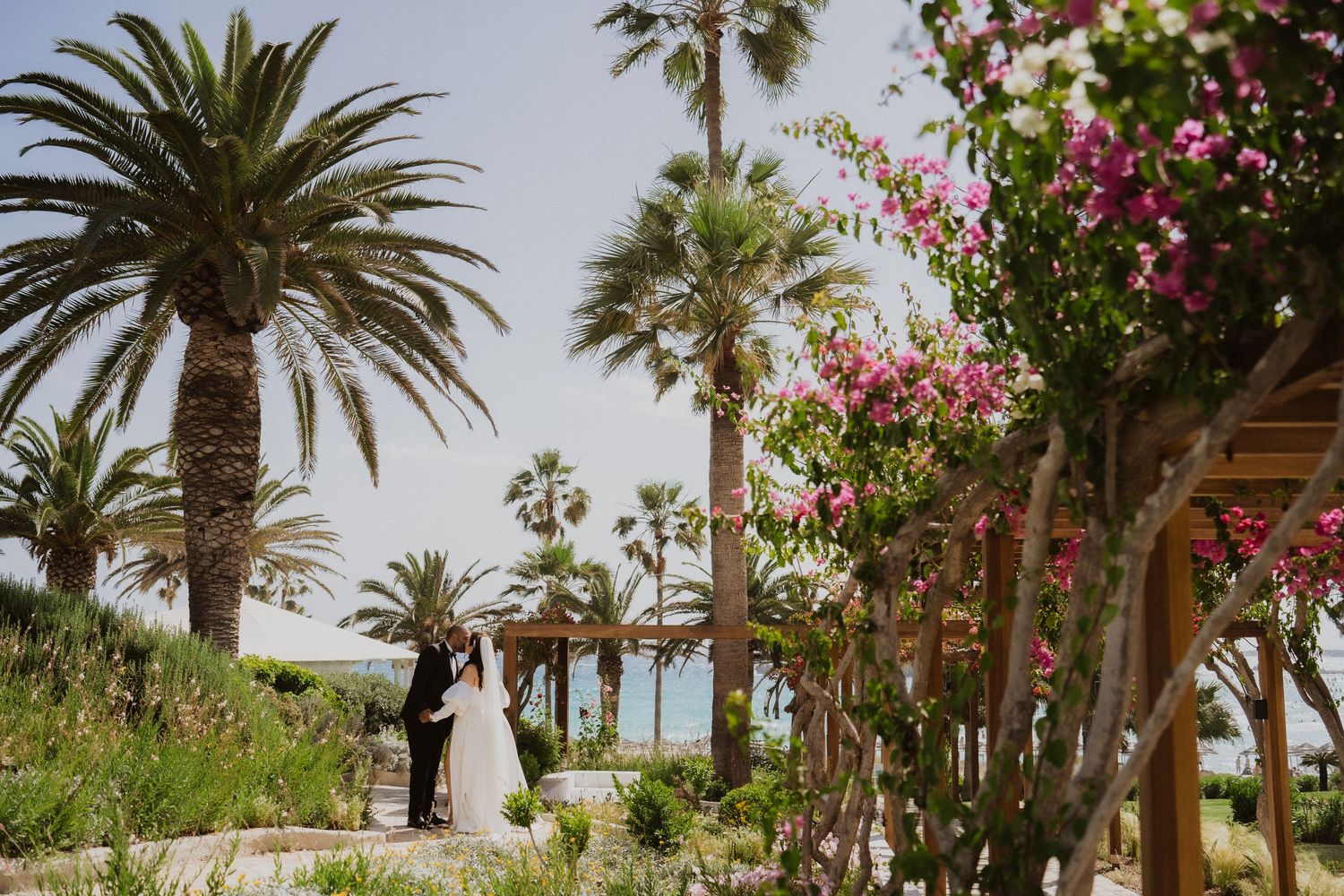 A wedding ceremony scene among palm trees and pink bougainvillea flowers with ocean views.