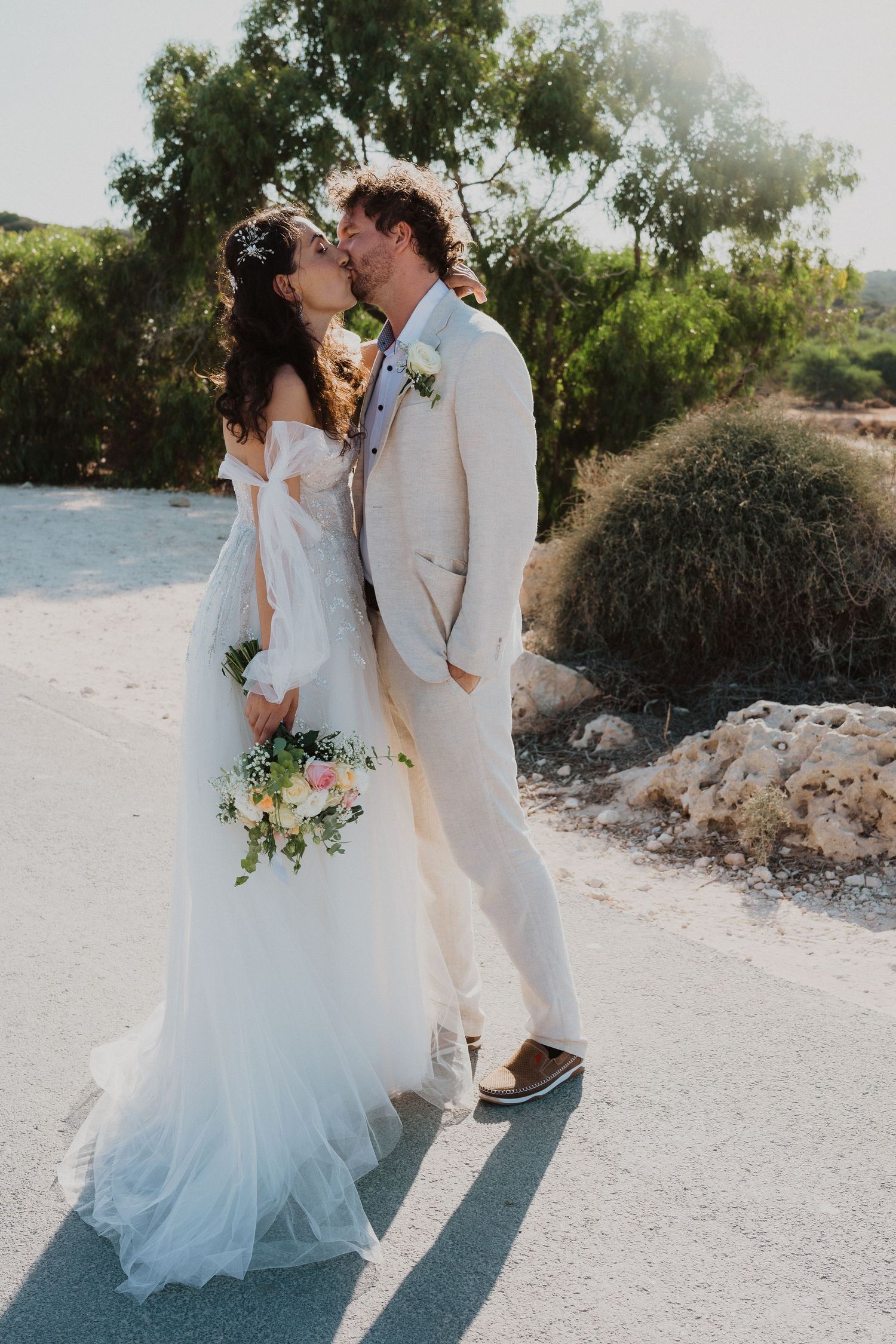Wedding couple sharing a romantic kiss outdoors in elegant white attire.
