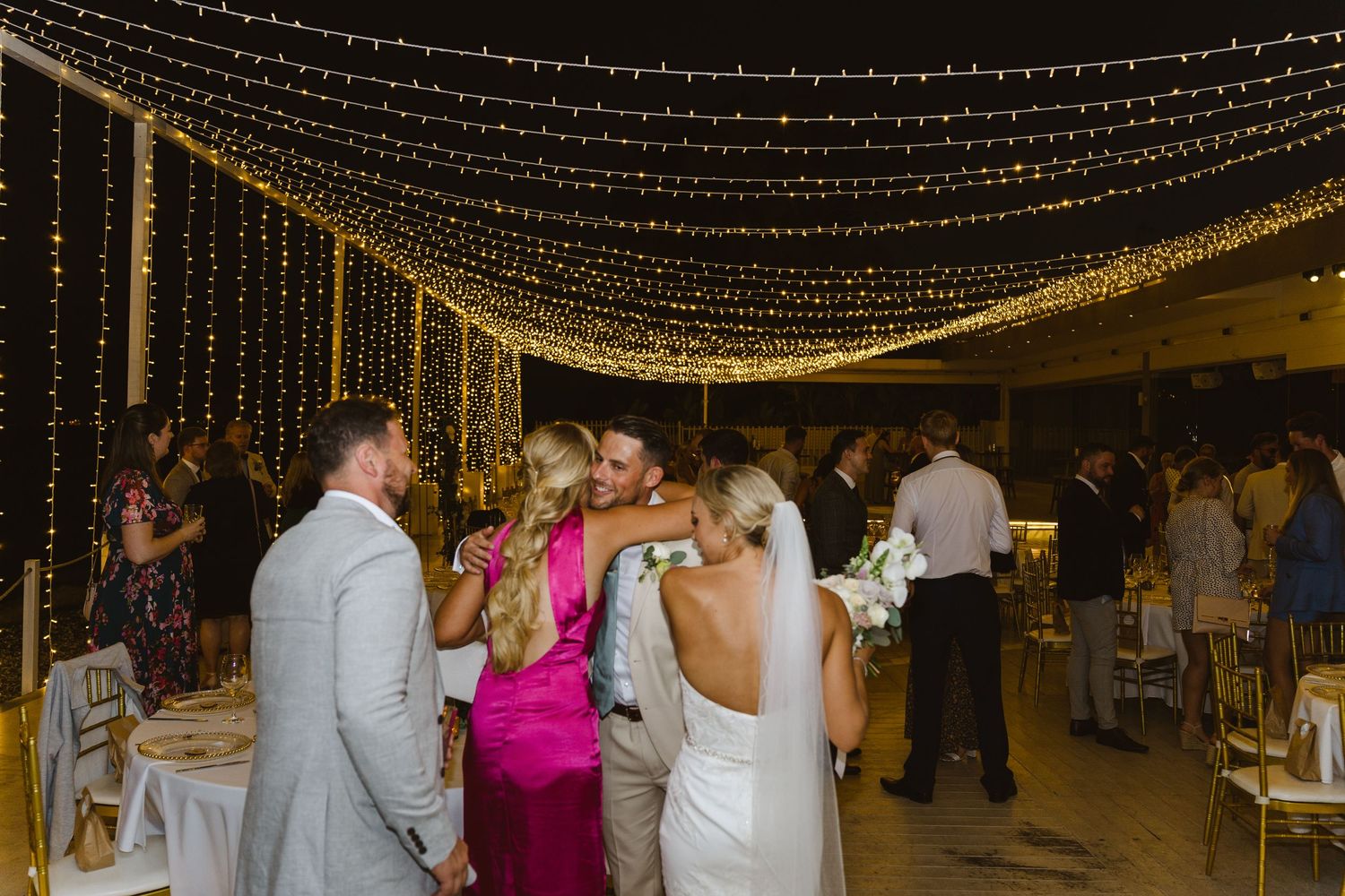 Wedding celebration under golden string light canopy with guests dancing and socializing.