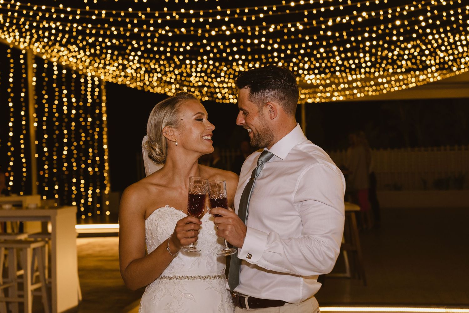 A romantic moment captured between newlyweds sharing drinks under a magical light display.