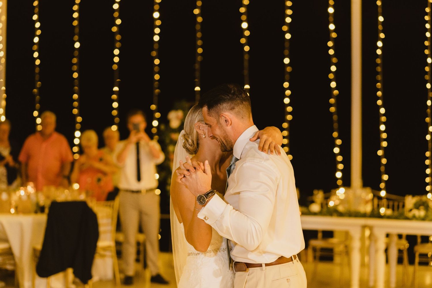 A romantic wedding dance moment captured under glowing string lights at an evening reception.
